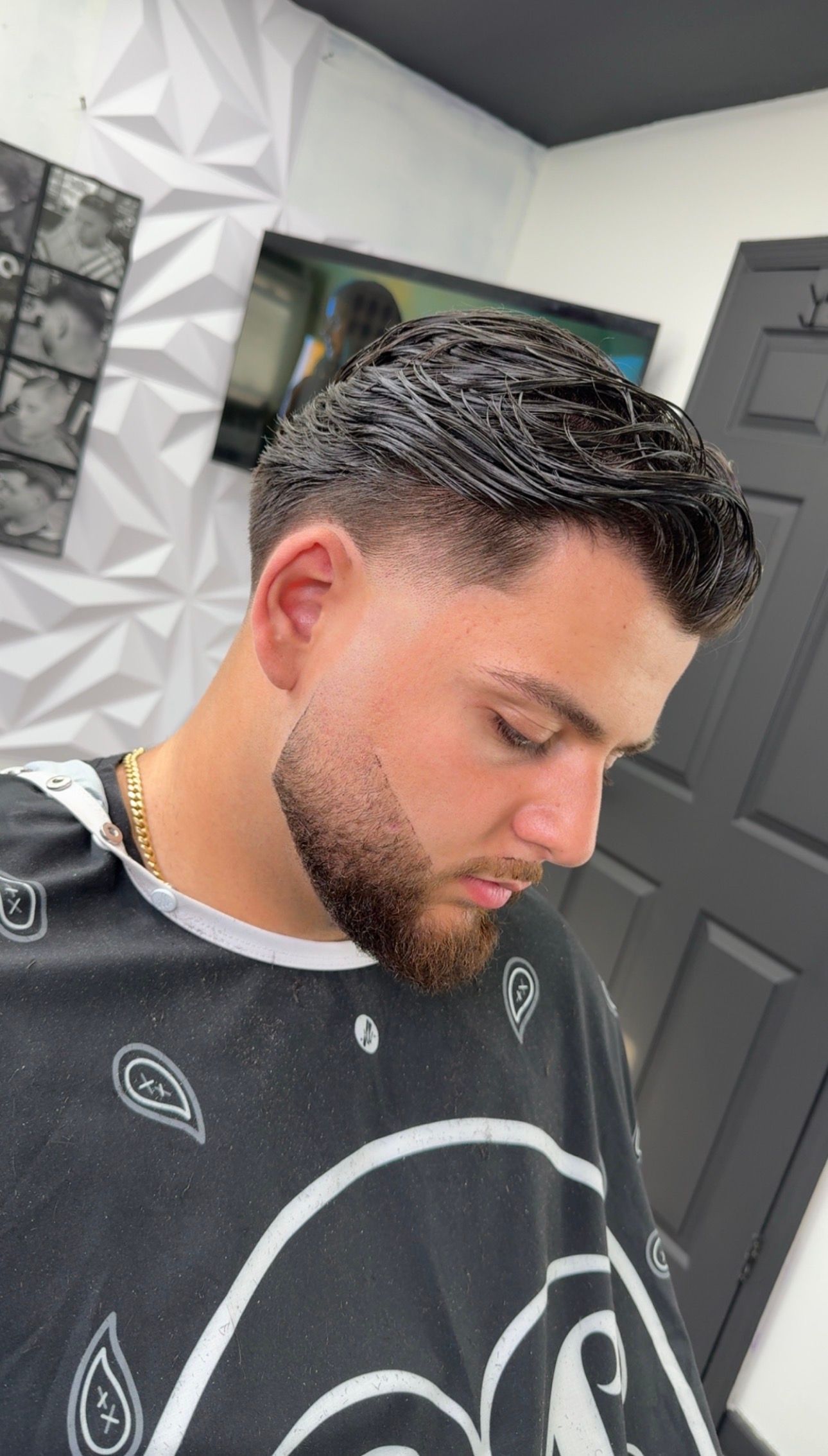 Man with a fresh haircut and beard in a barber shop. He is wearing a cape.