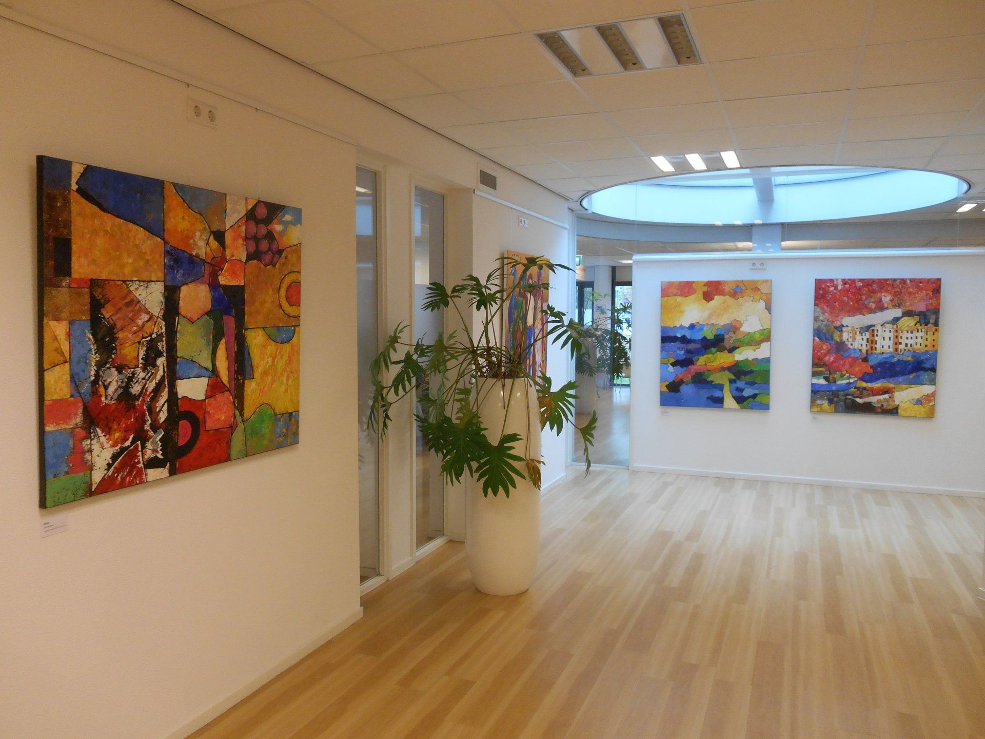 Een gang met schilderijen aan de muur en een potplant.