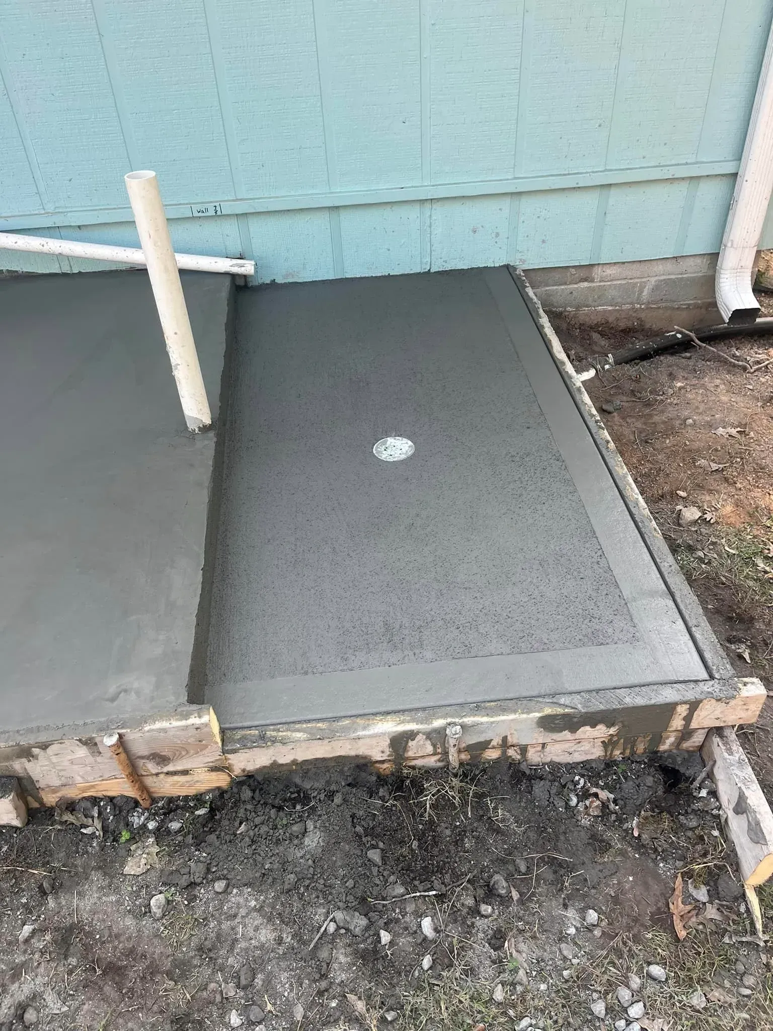 Freshly poured concrete slab next to a building's light blue siding and a white downspout.