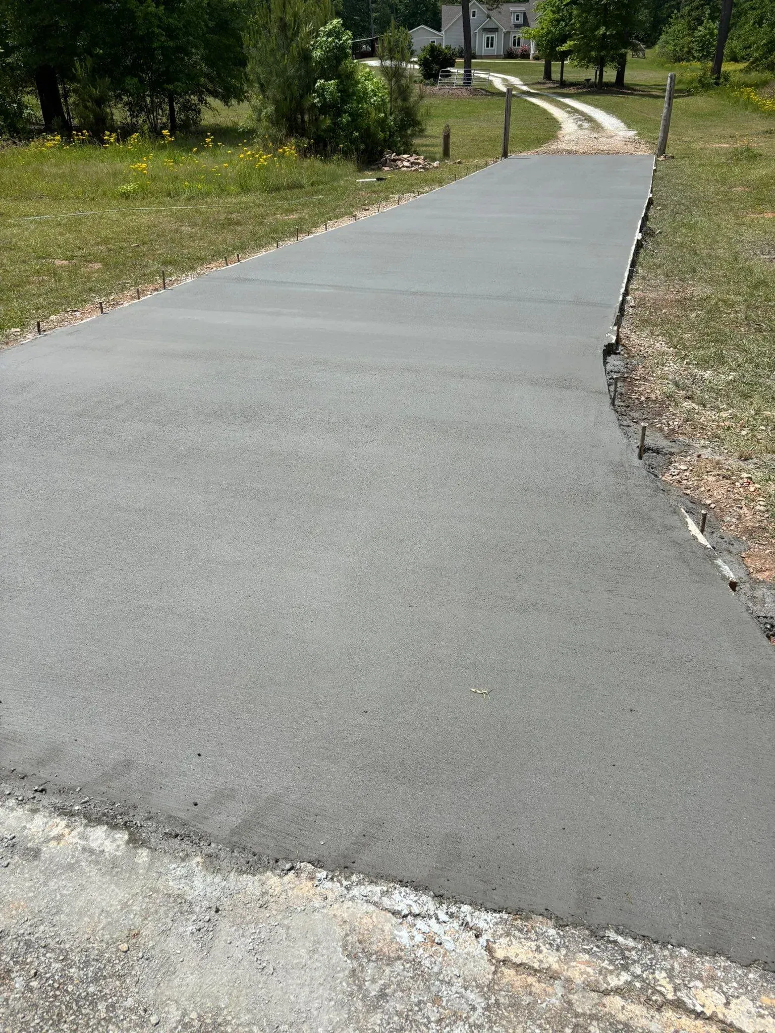 A newly paved asphalt driveway curves through grass towards a house in the background.