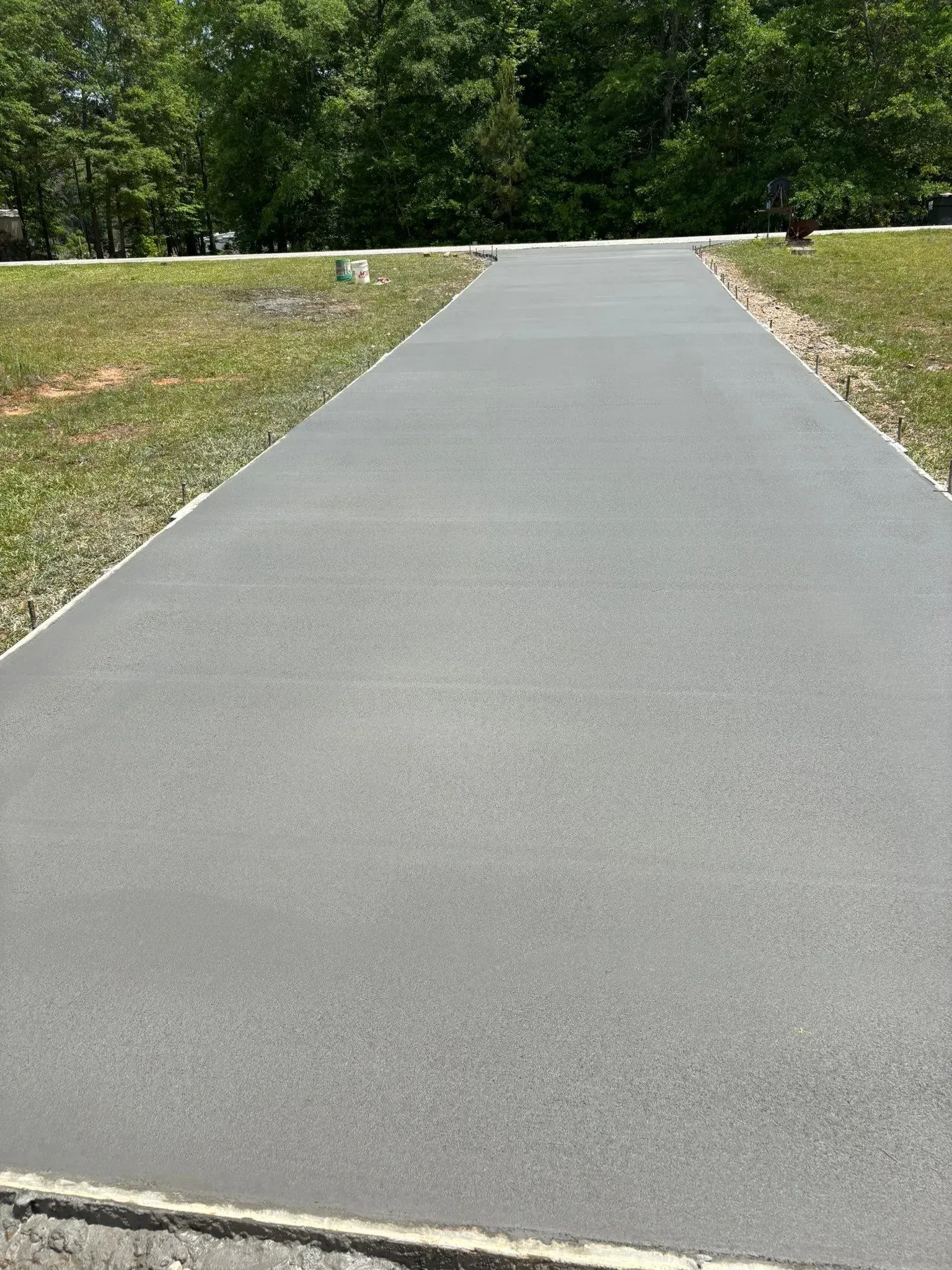A gray paved walkway surrounded by grass, leading towards trees.
