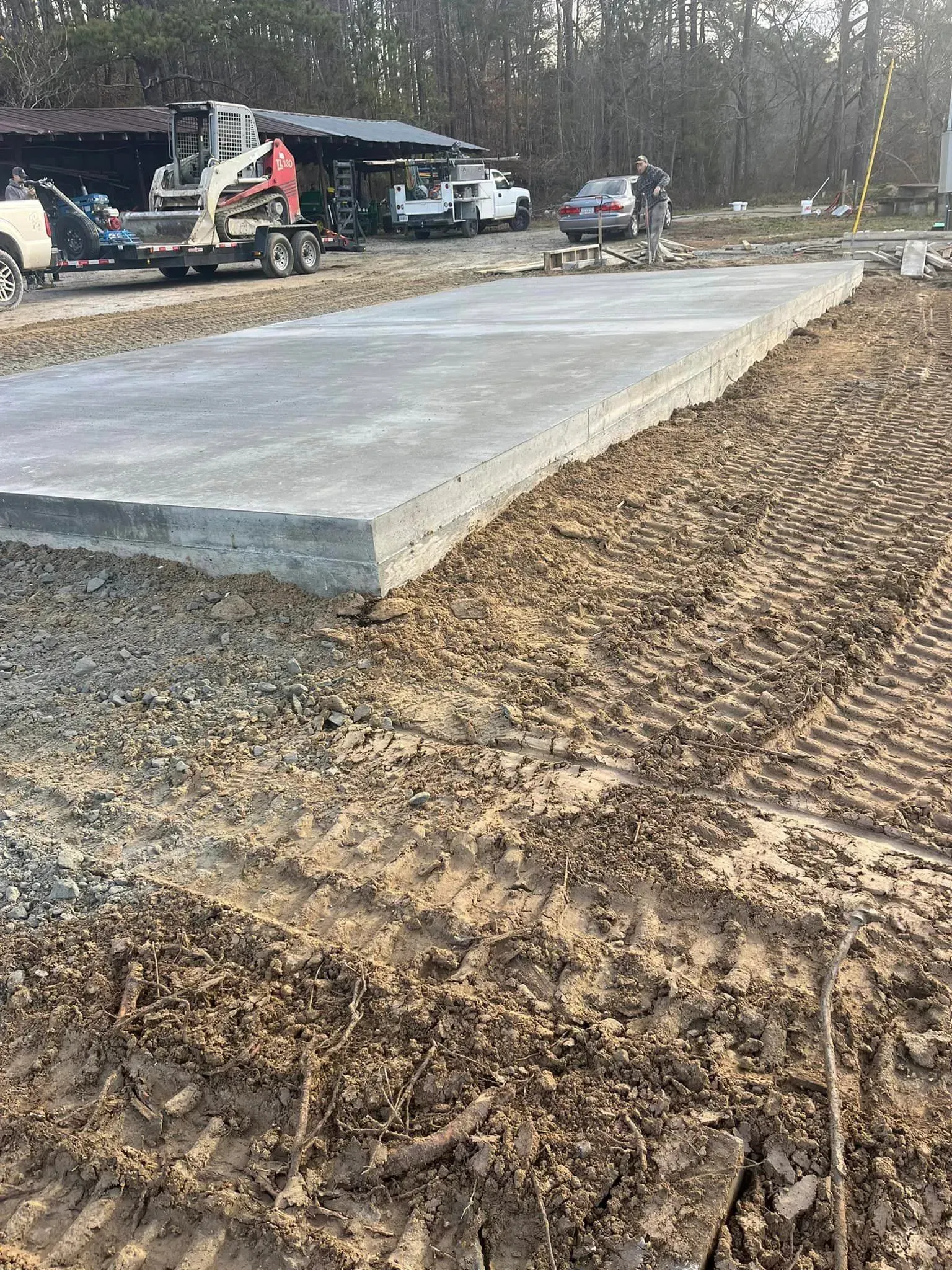 Concrete slab under construction; dirt and machinery surround the rectangular foundation in an outdoor setting.