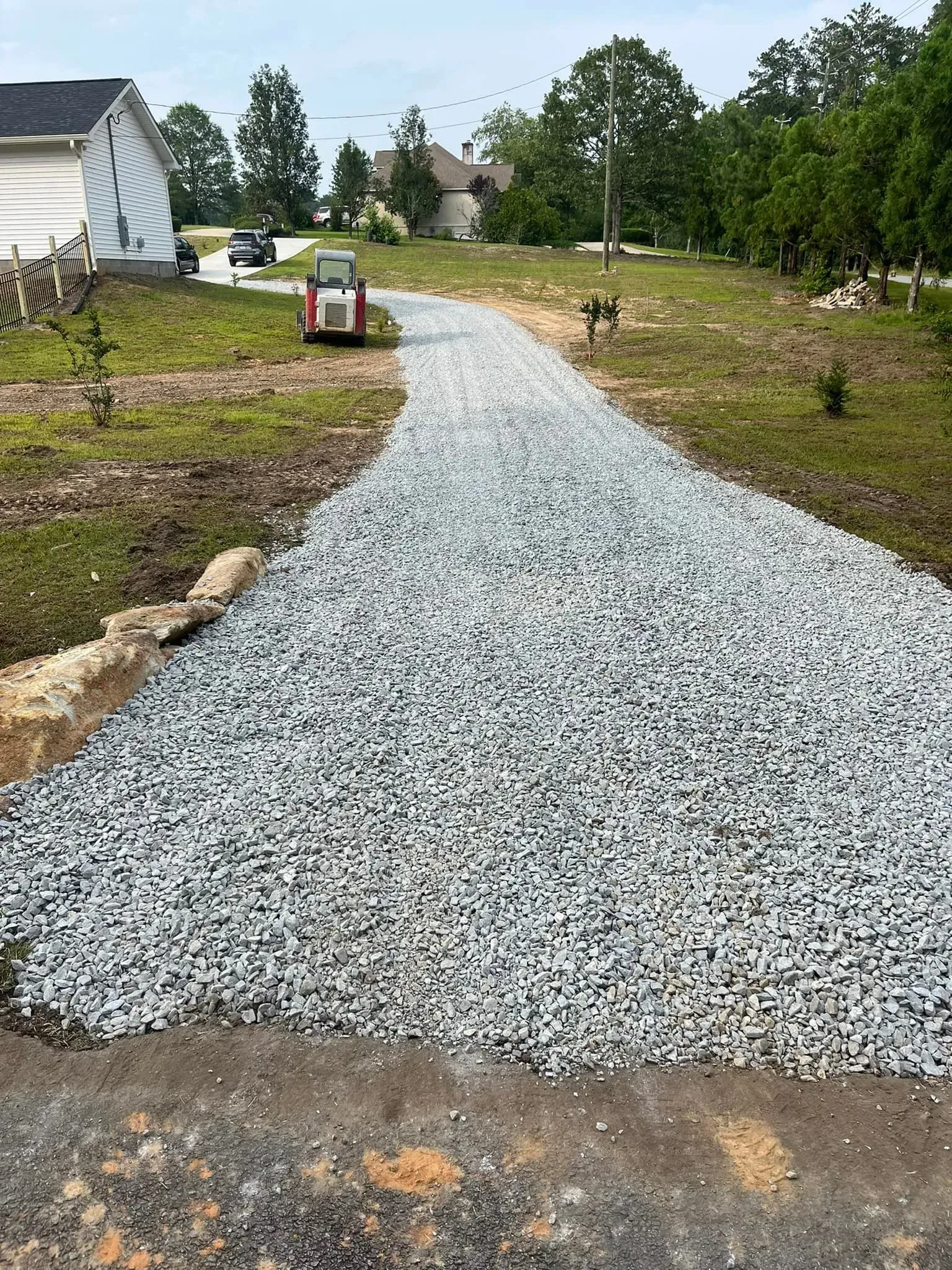 Gravel driveway leads uphill to a house; a small construction vehicle is parked on it.