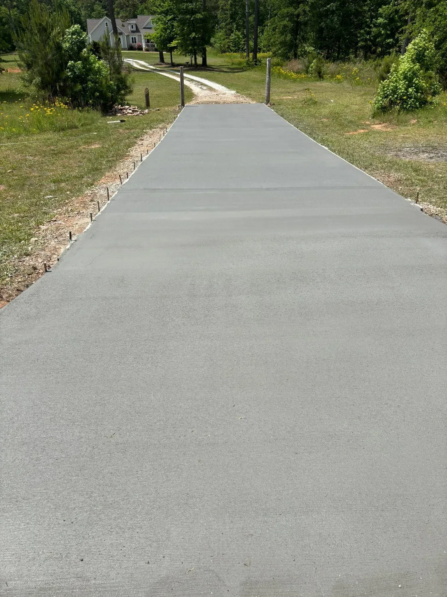 Gray concrete driveway leading to a house, bordered by gravel and grass.