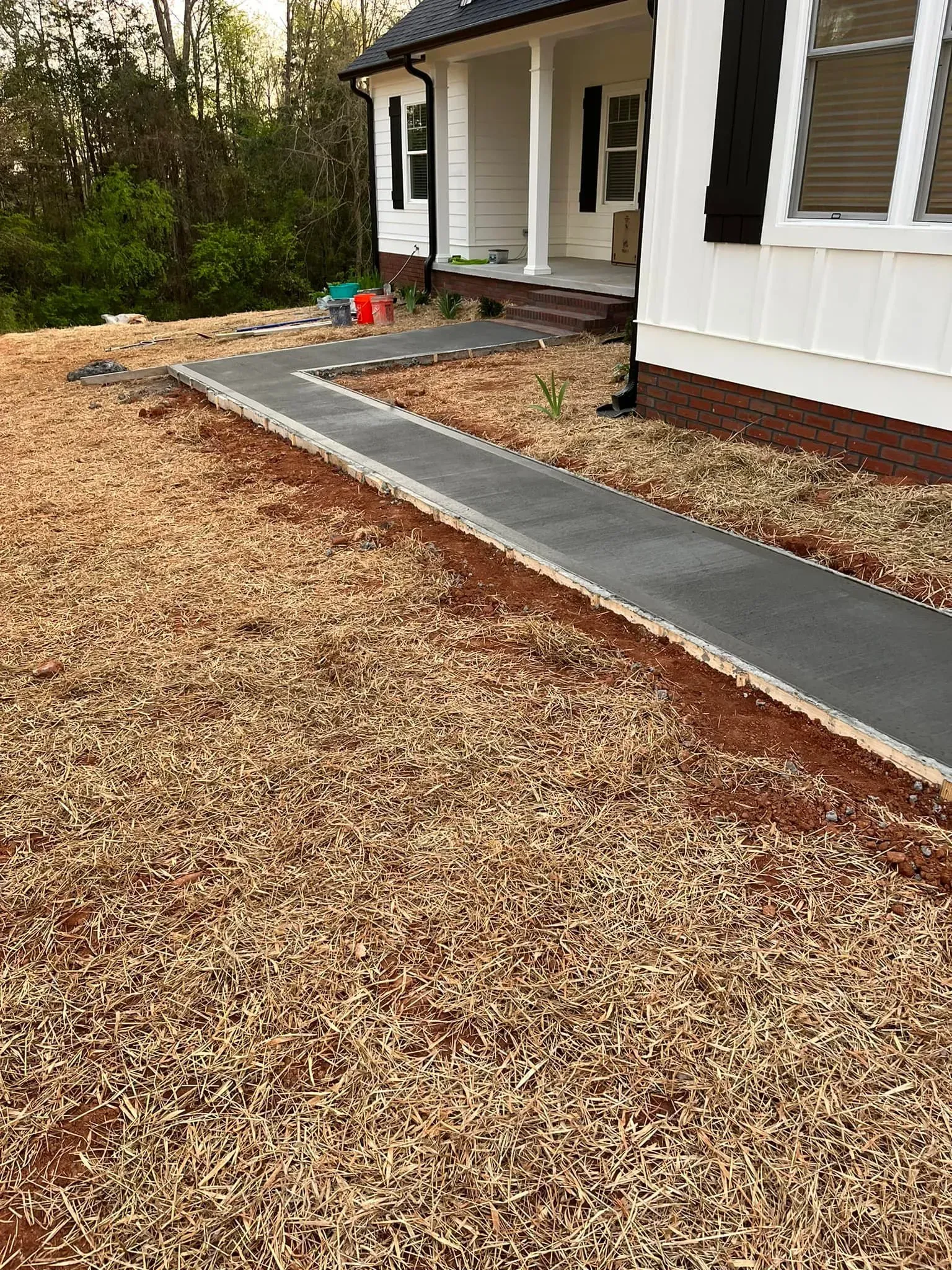 A concrete walkway leads to a white house with a porch. Dry, brown grass surrounds the walkway.