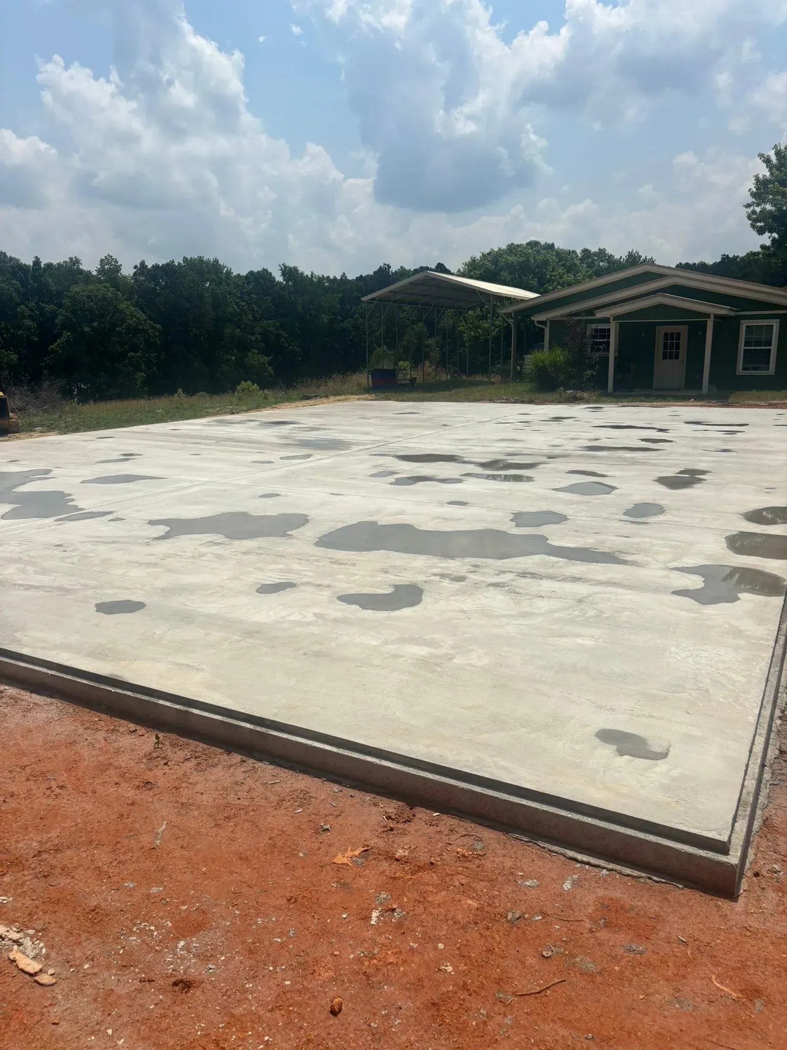 Newly poured concrete slab with a building and trees in the background.