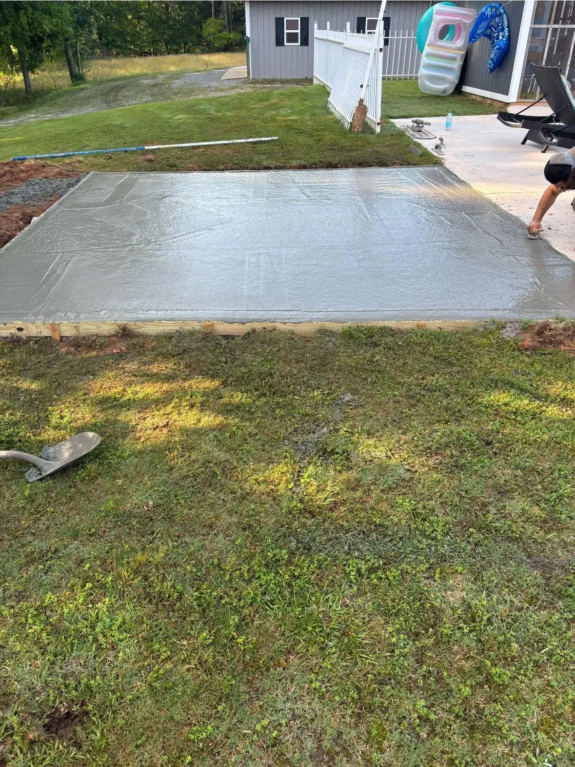 Freshly poured concrete patio with wooden frame, surrounded by grass. Person near the edge.