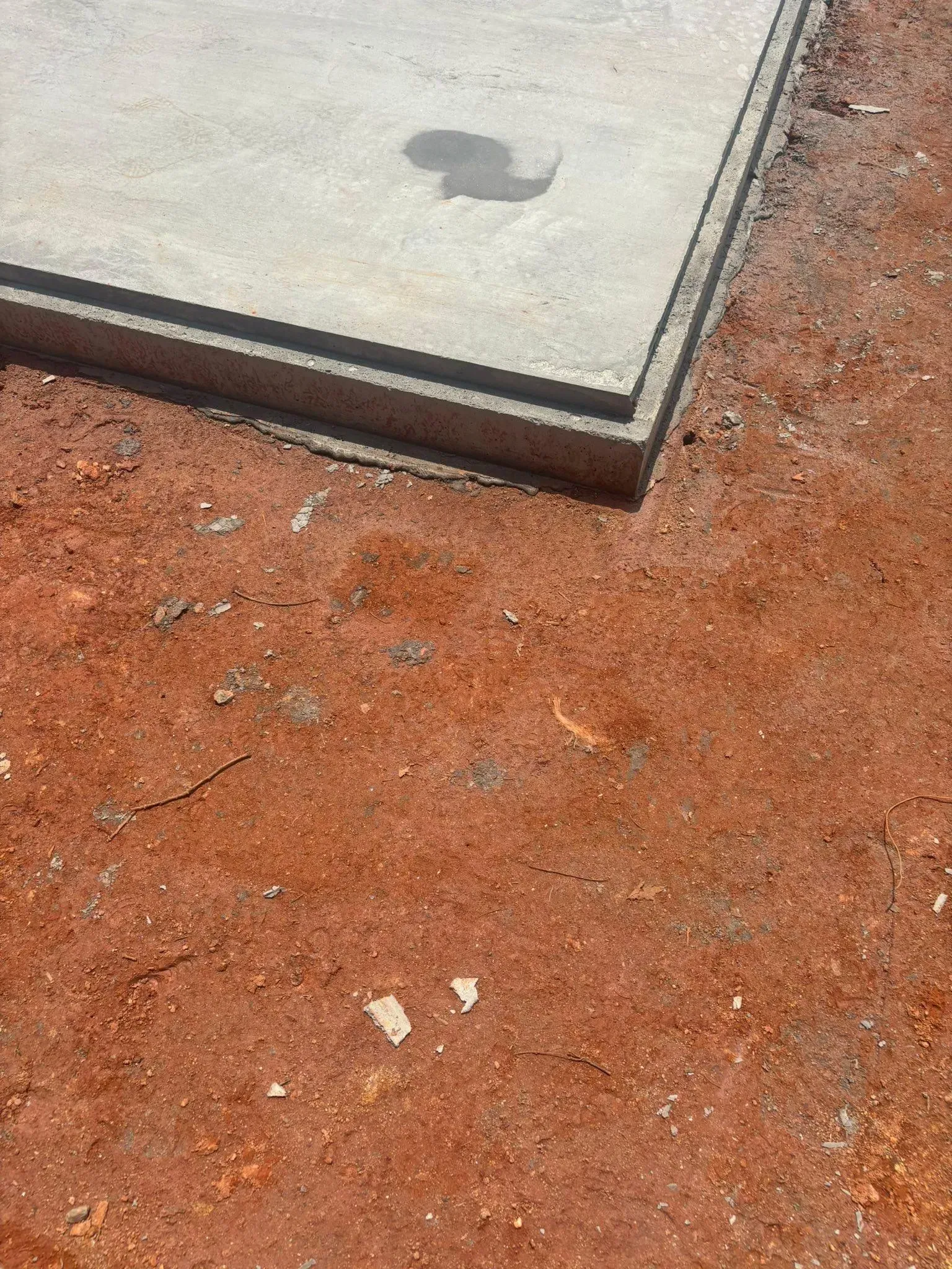 Concrete pad with a water stain on red dirt ground.