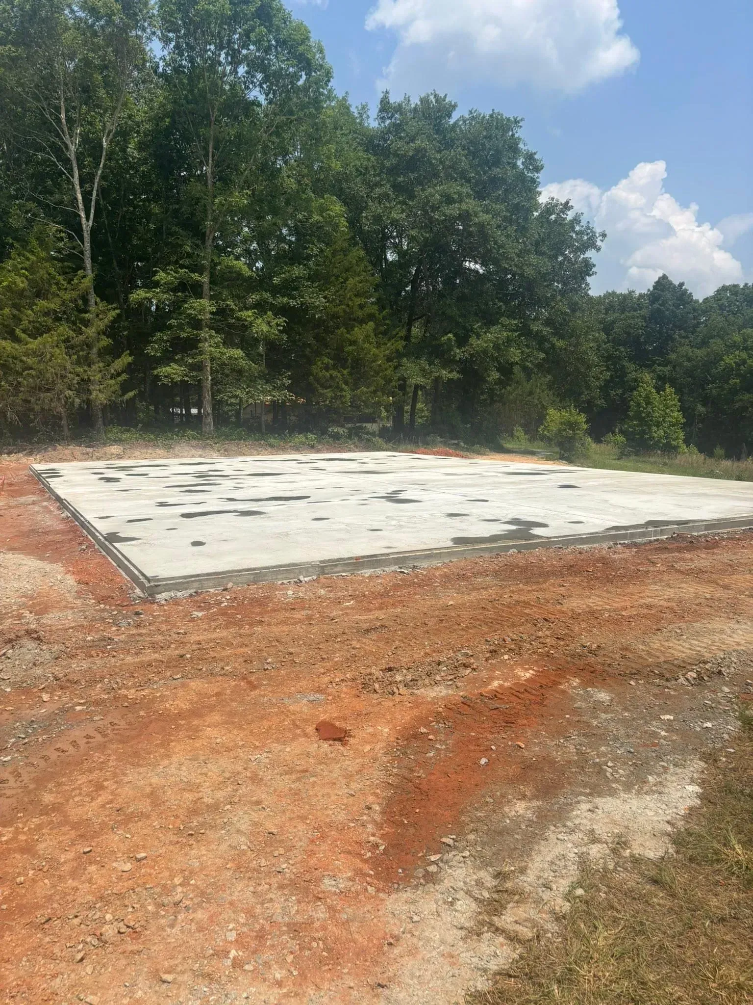 Concrete slab foundation outdoors, surrounded by red dirt and trees, under a blue sky.