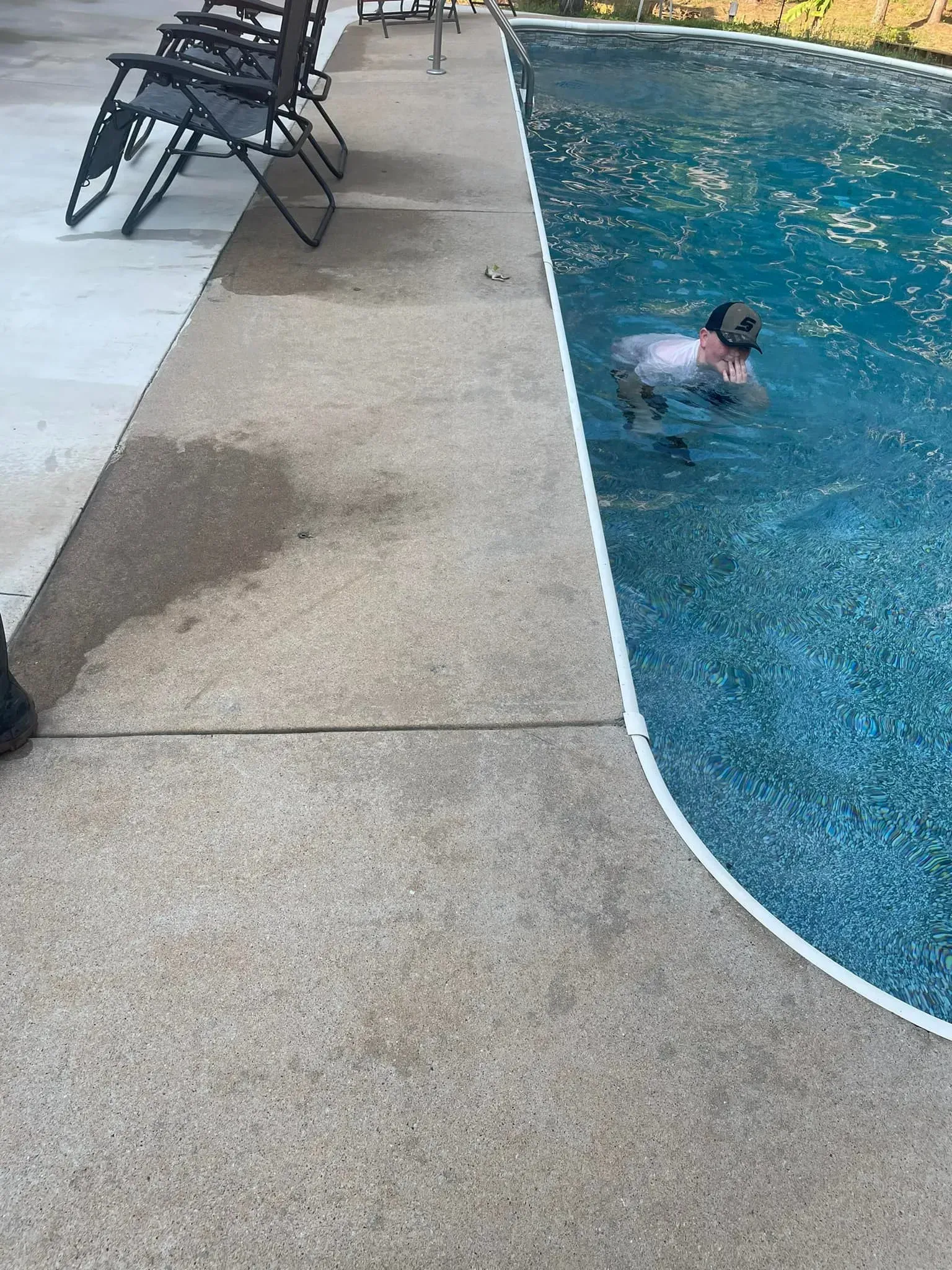 Child swimming in a blue pool, next to a concrete deck with chairs.