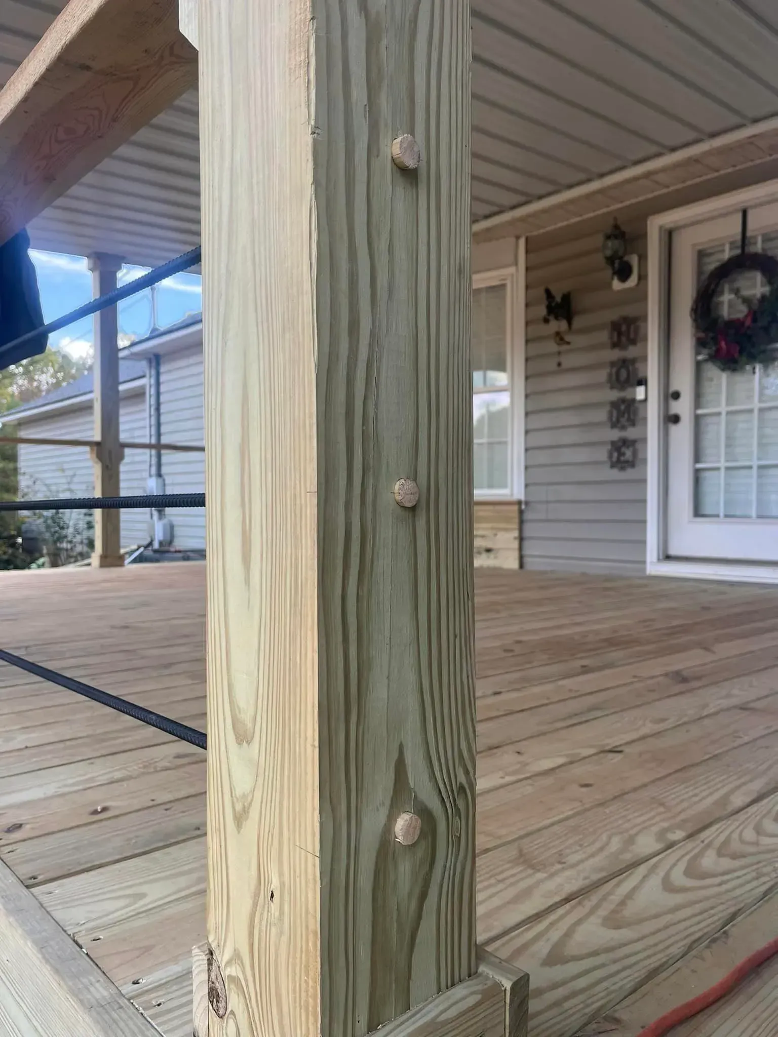Wooden porch post with three wooden plugs, on a wooden deck.