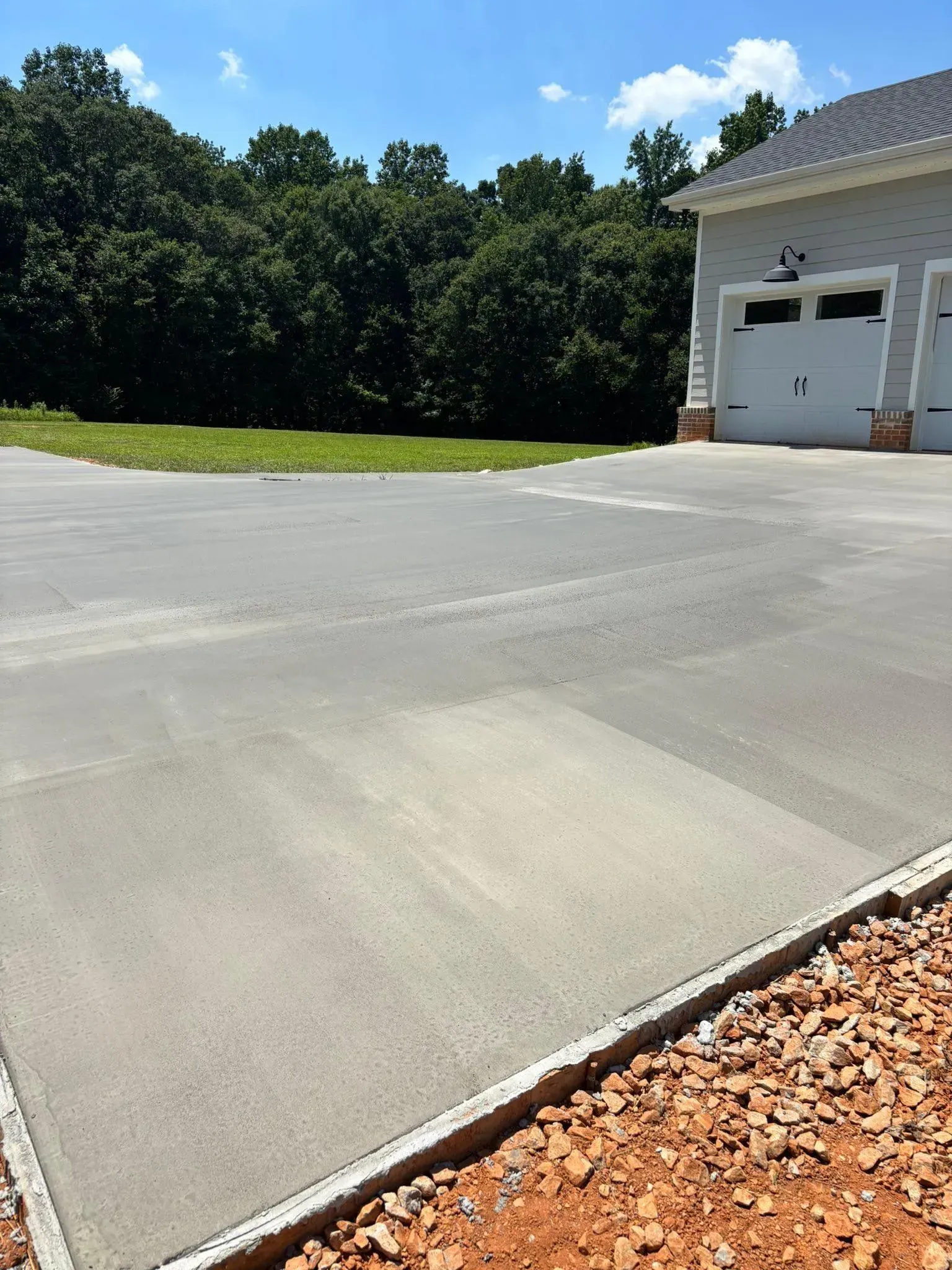 Concrete driveway leading to a garage, surrounded by landscaping and trees, under a blue sky.