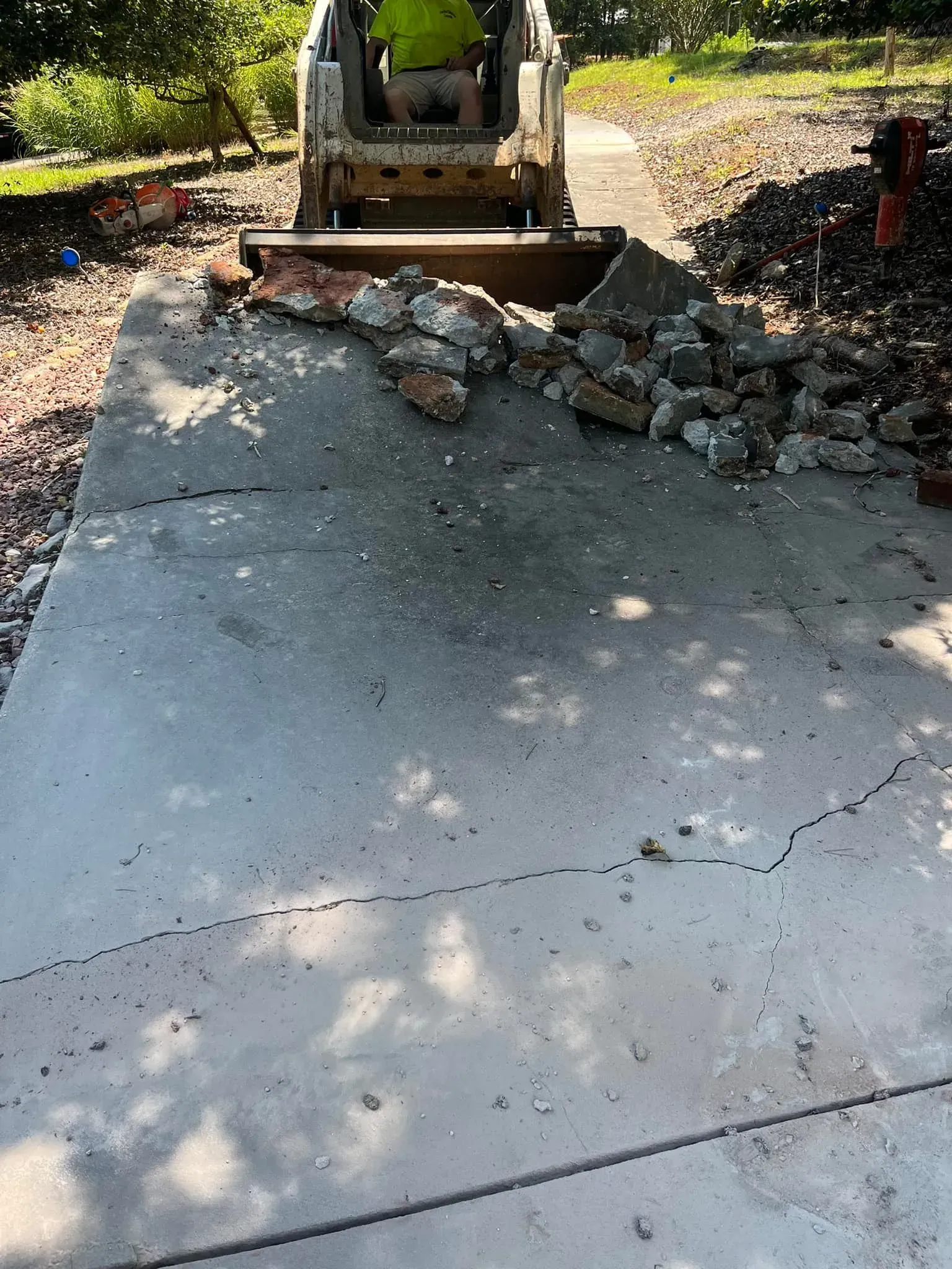 Skid steer removing brick debris from a cracked concrete driveway.