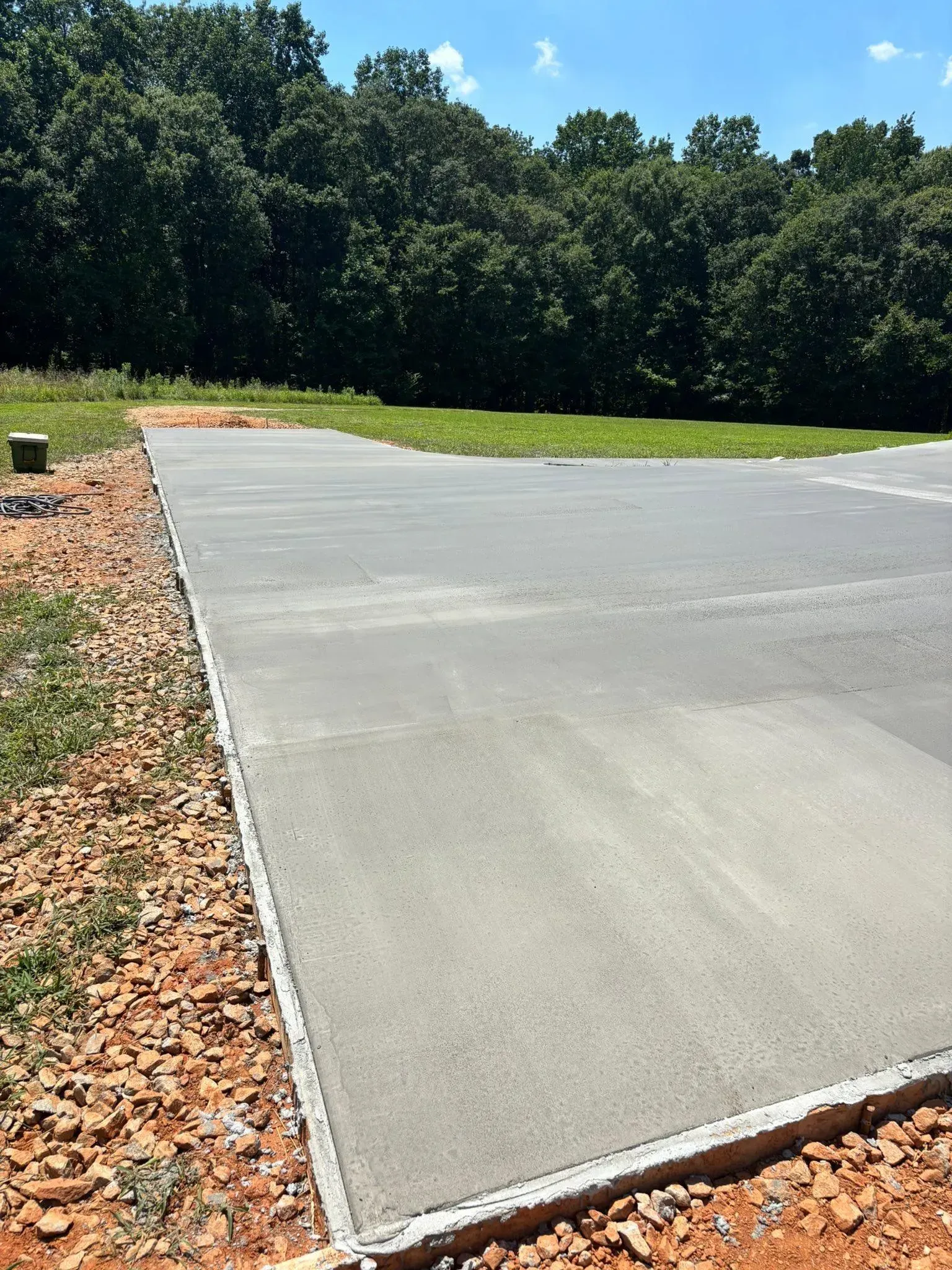 Newly poured concrete driveway with tree line in the background.