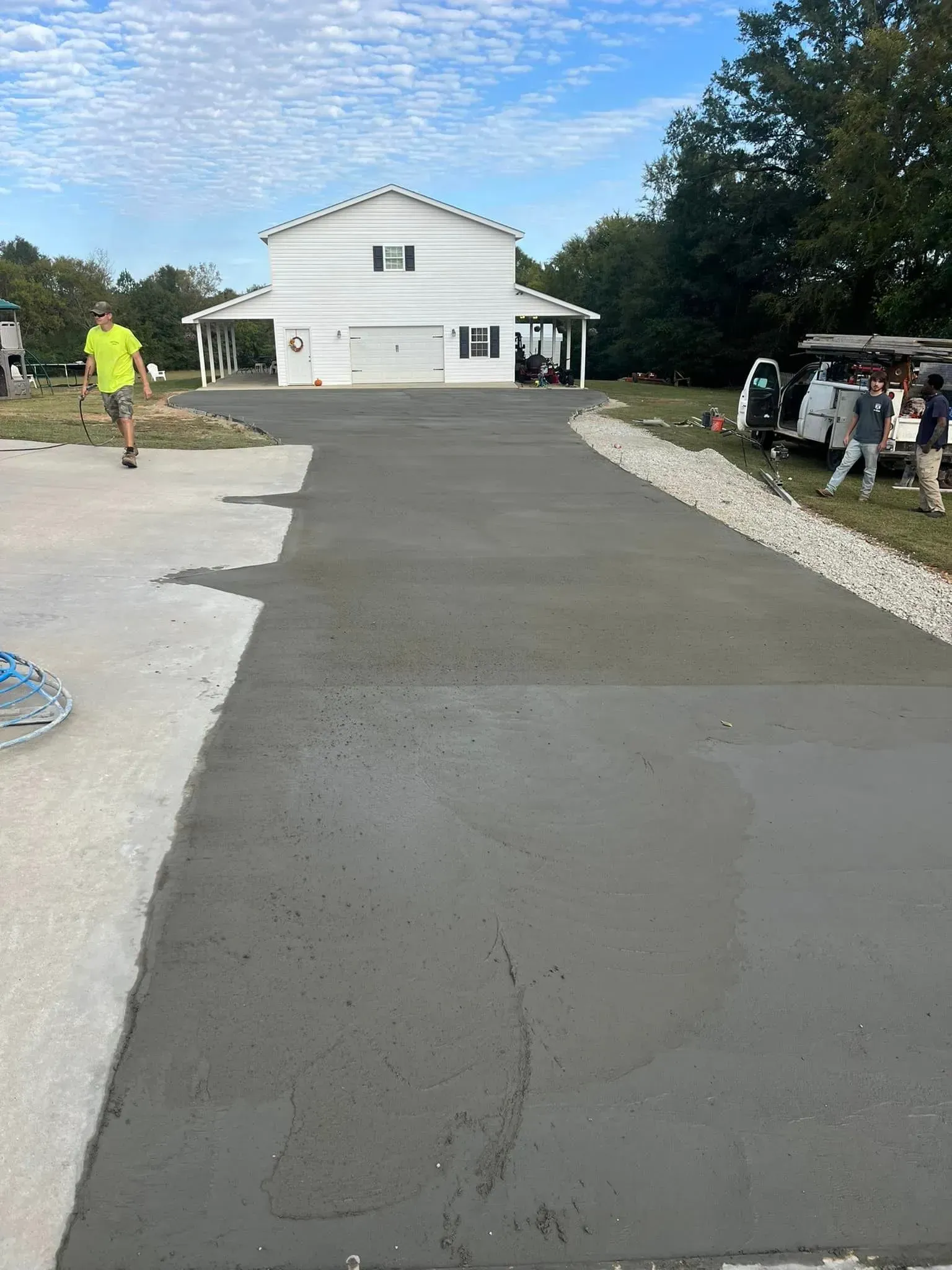 New concrete driveway leading to a white house. Workers in the distance.