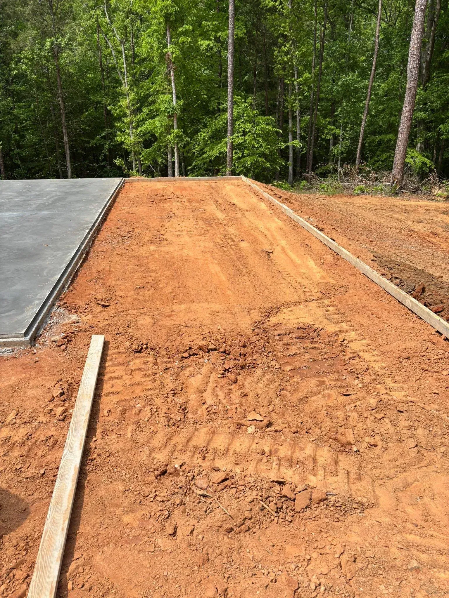 Dirt path alongside a concrete slab, edged with wooden boards, backed by a line of trees.