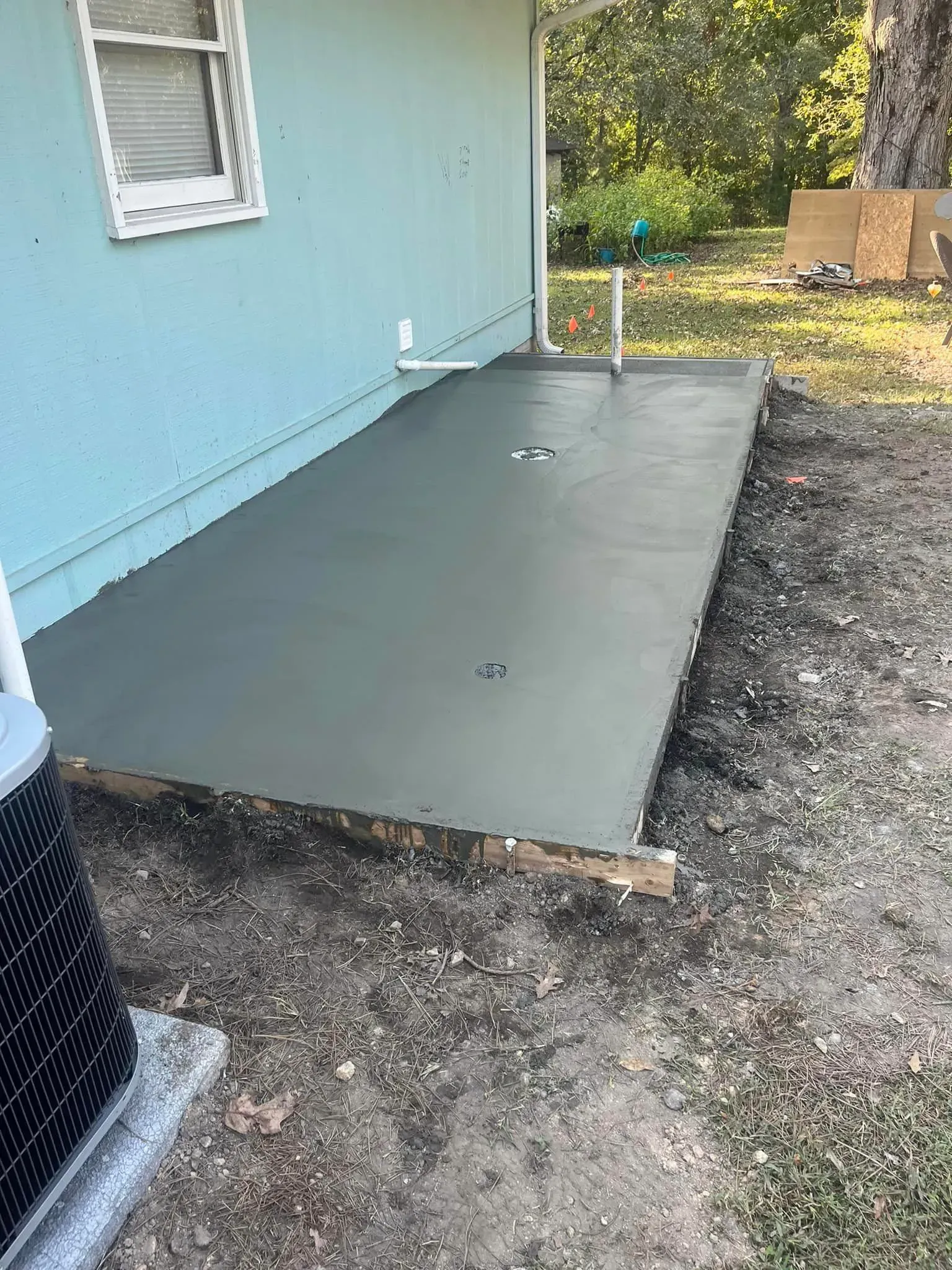 Freshly poured gray concrete slab next to a light blue building, with the AC unit visible.