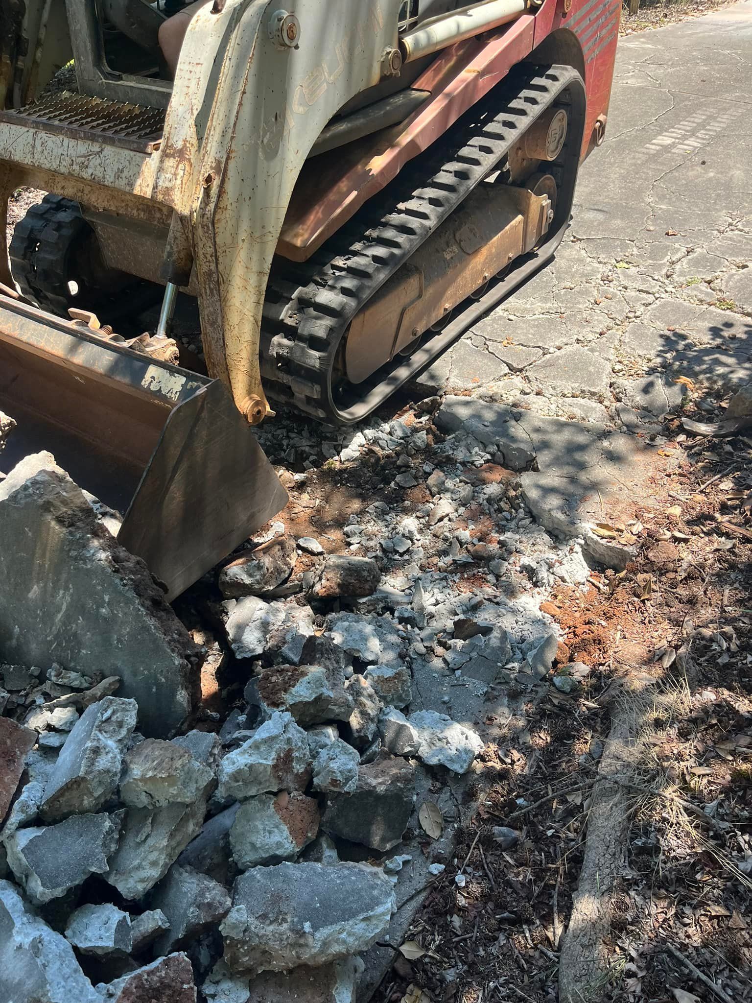 Skid steer removing broken concrete on a paved area.