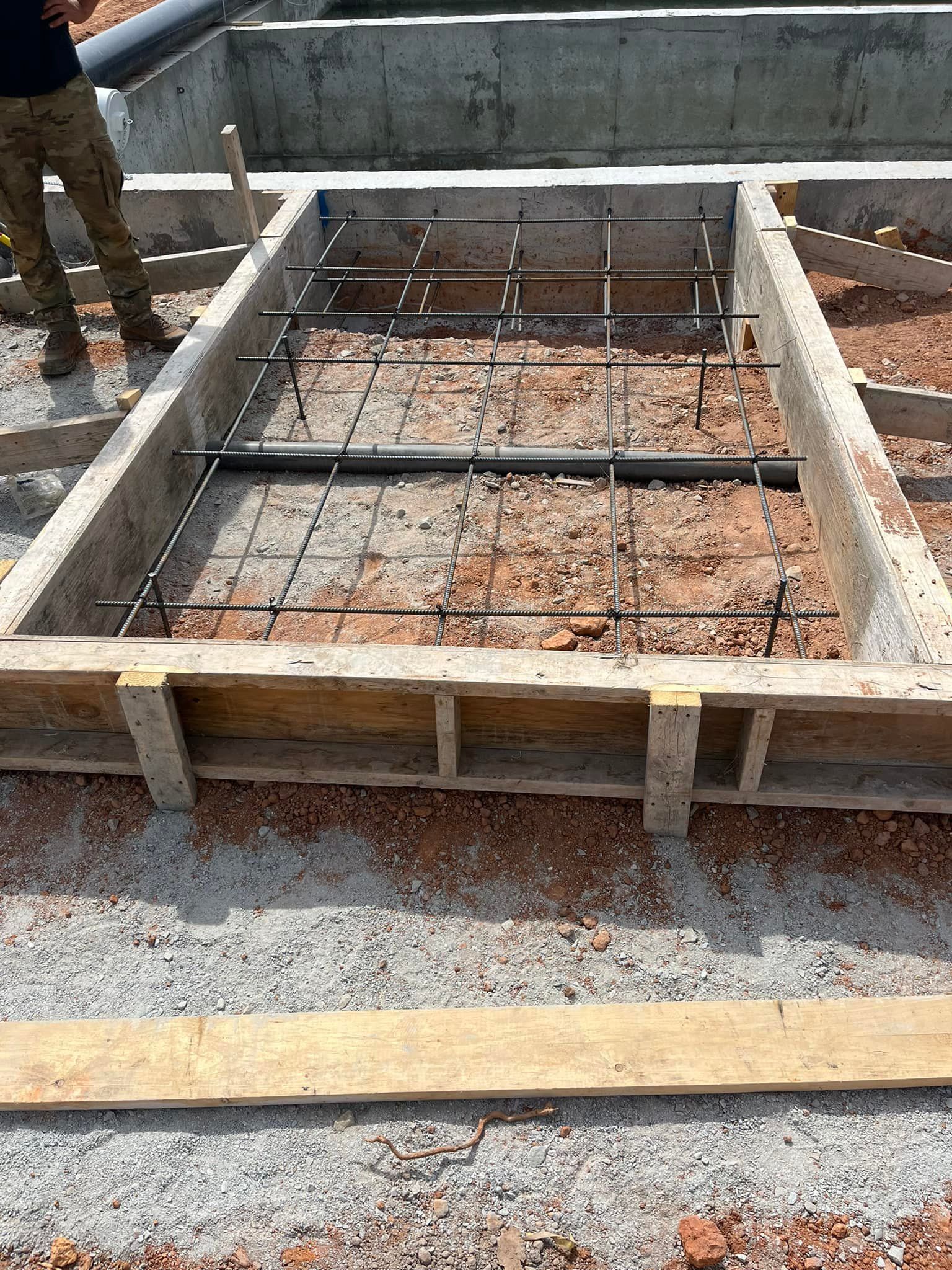 Concrete foundation with rebar grid, wooden frame, construction site.