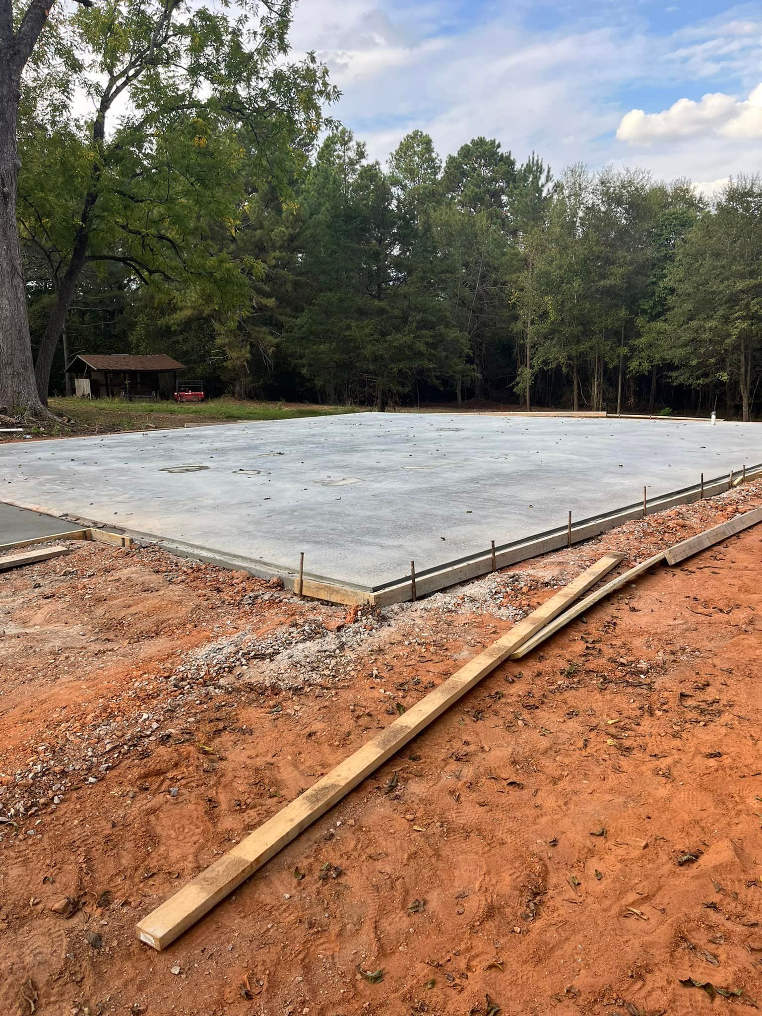 Newly poured concrete foundation, wooden forms, and soil, surrounded by trees.