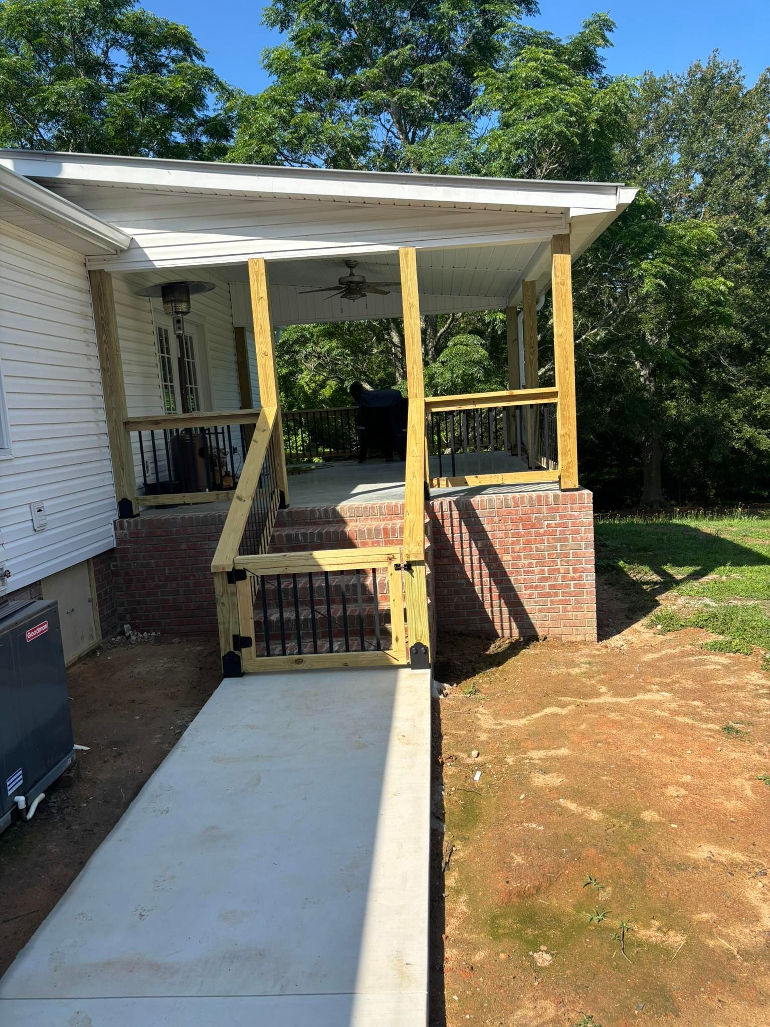 New porch with wooden frame and brick pillars; concrete walkway.
