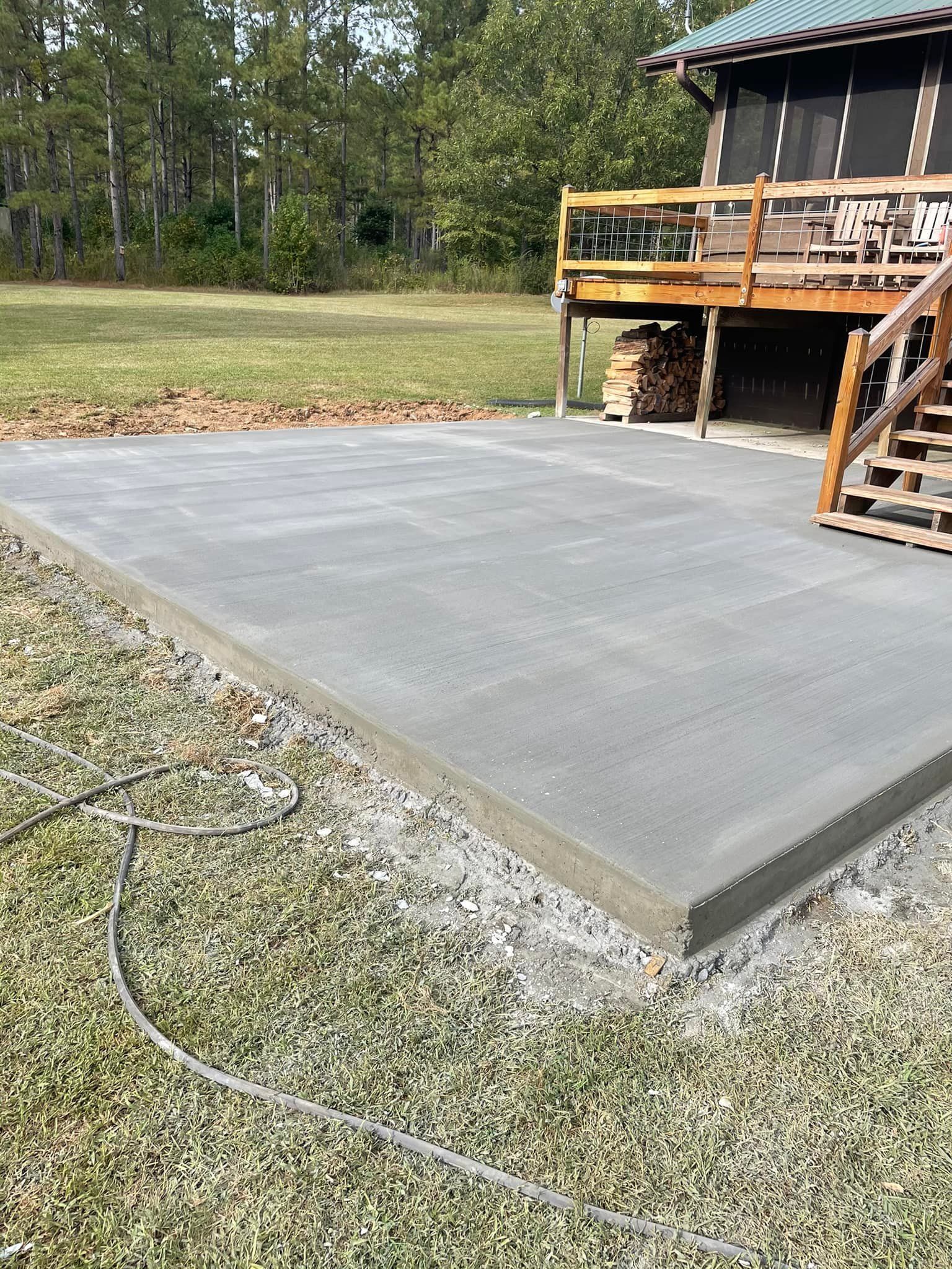 A freshly poured concrete patio next to a wooden deck with a grassy yard.