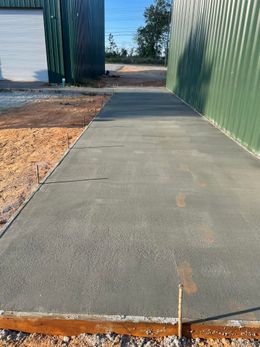 Concrete sidewalk between green and white buildings, gravel on sides.