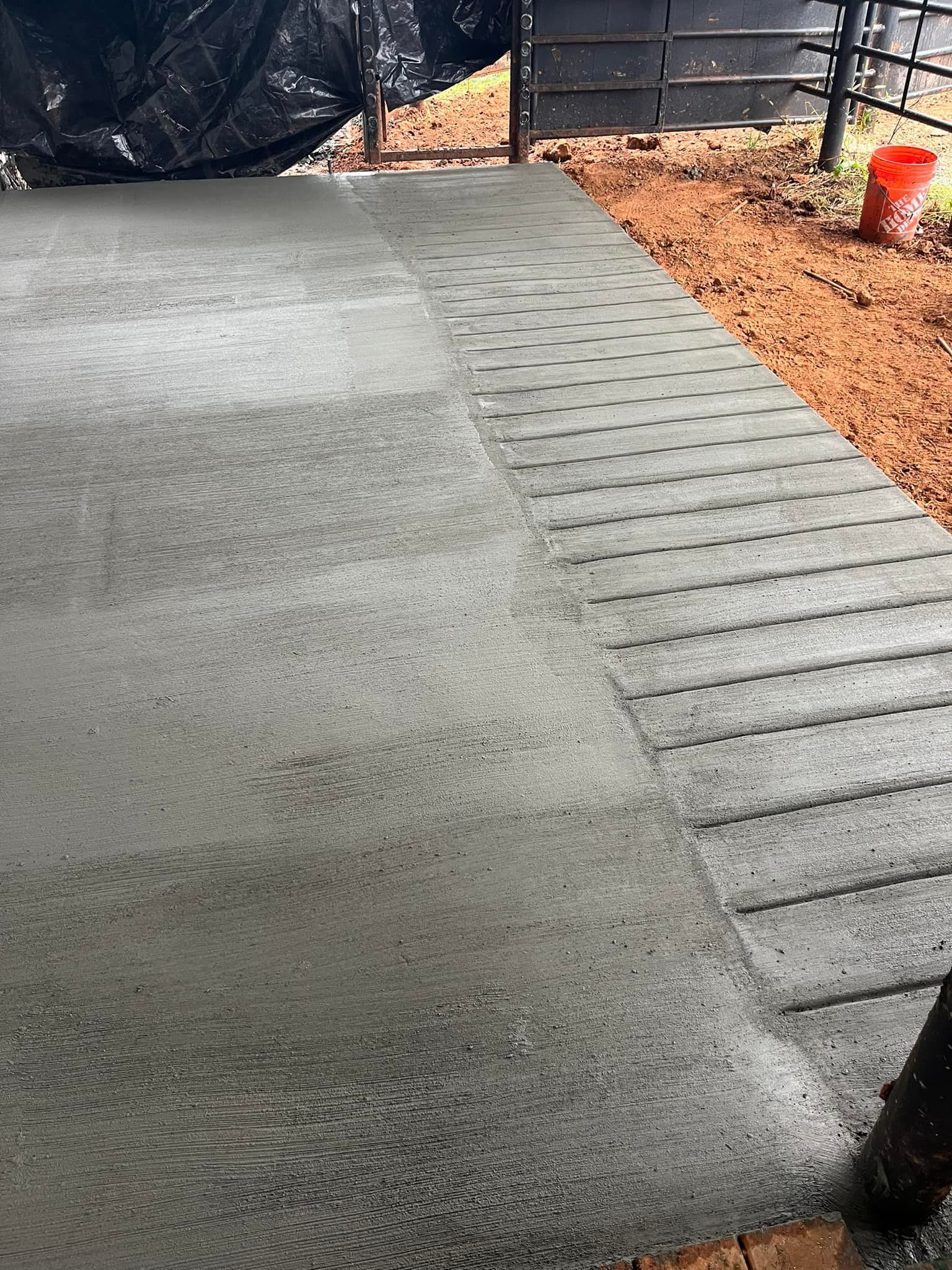 Newly poured concrete with textured, grid-like section; adjacent to a dirt area; small orange bucket visible.