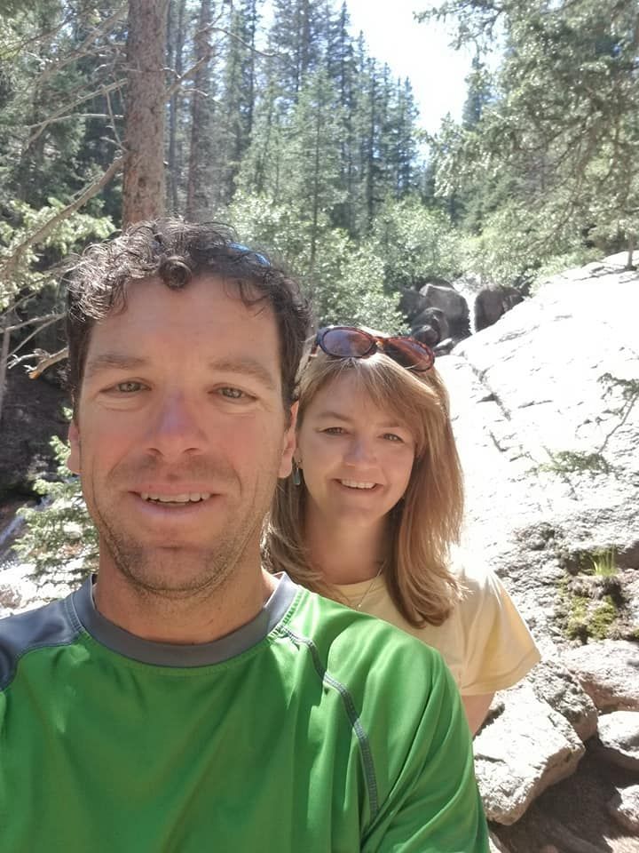 A man and a woman are posing for a picture in the woods.