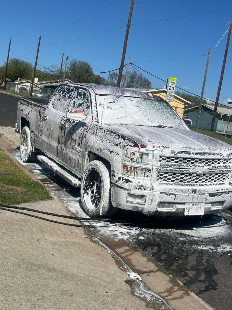 Pickup truck covered in white foam being washed on a street curb