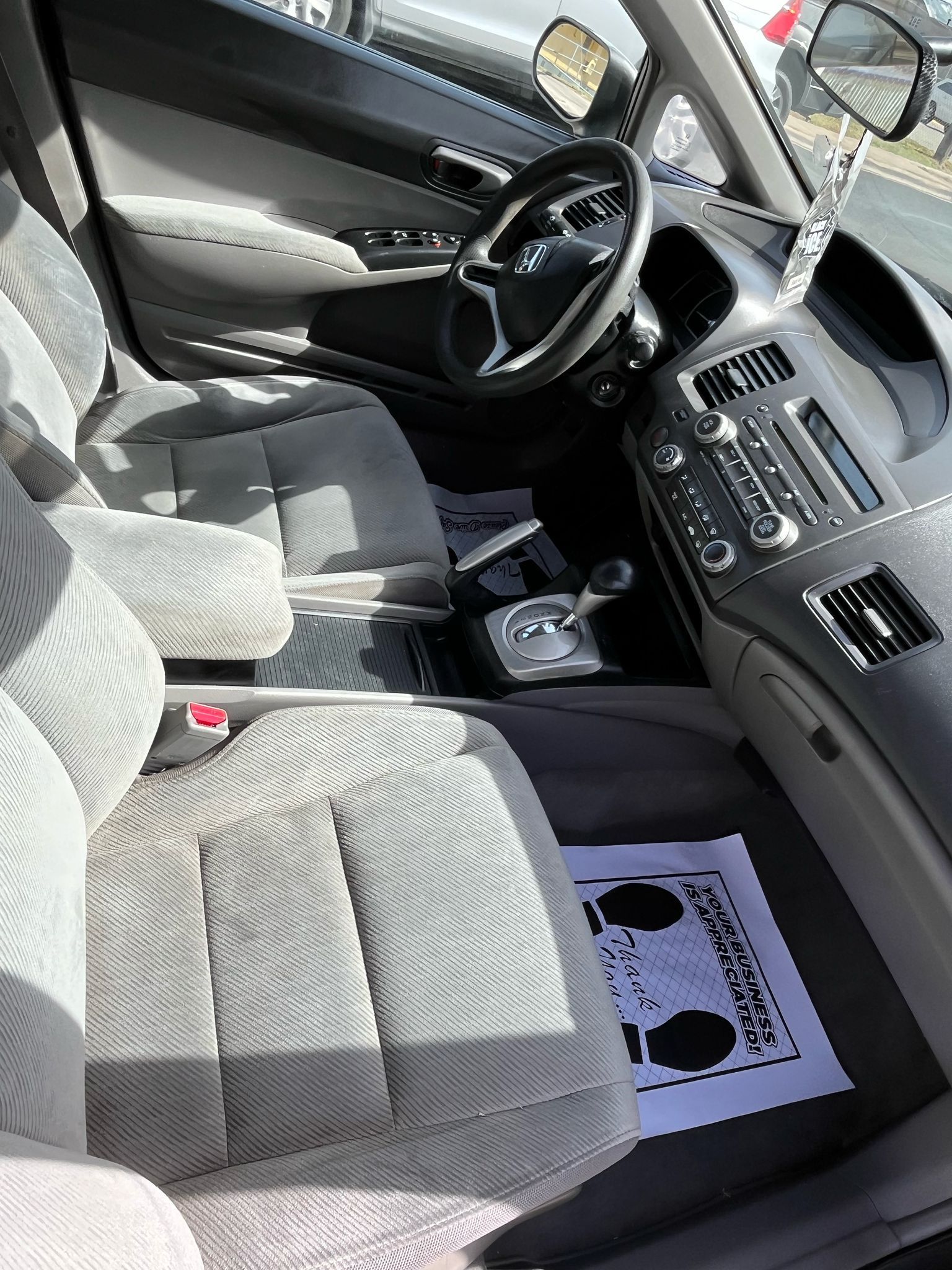 Front interior of a car with gray cloth seats, steering wheel, center console, and floor mat visible.