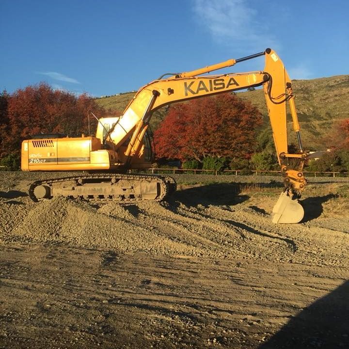 A yellow excavator is digging a hole in front of a building under construction.