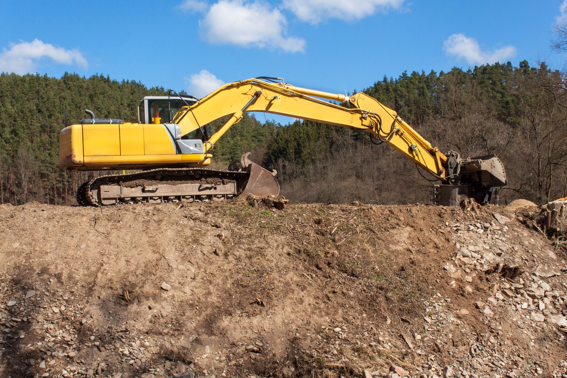 A yellow excavator is digging a hole in a dirt field.
