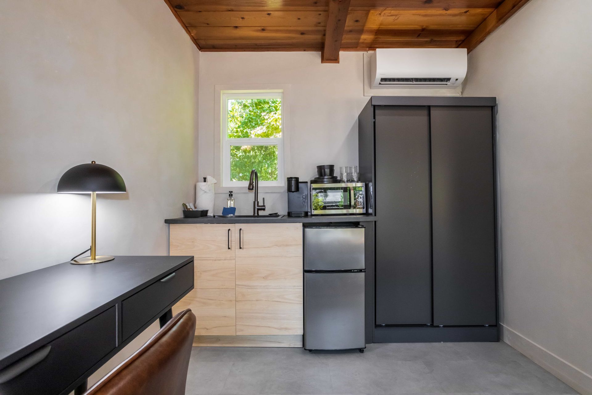 A small kitchen with a desk , chair , refrigerator and microwave.