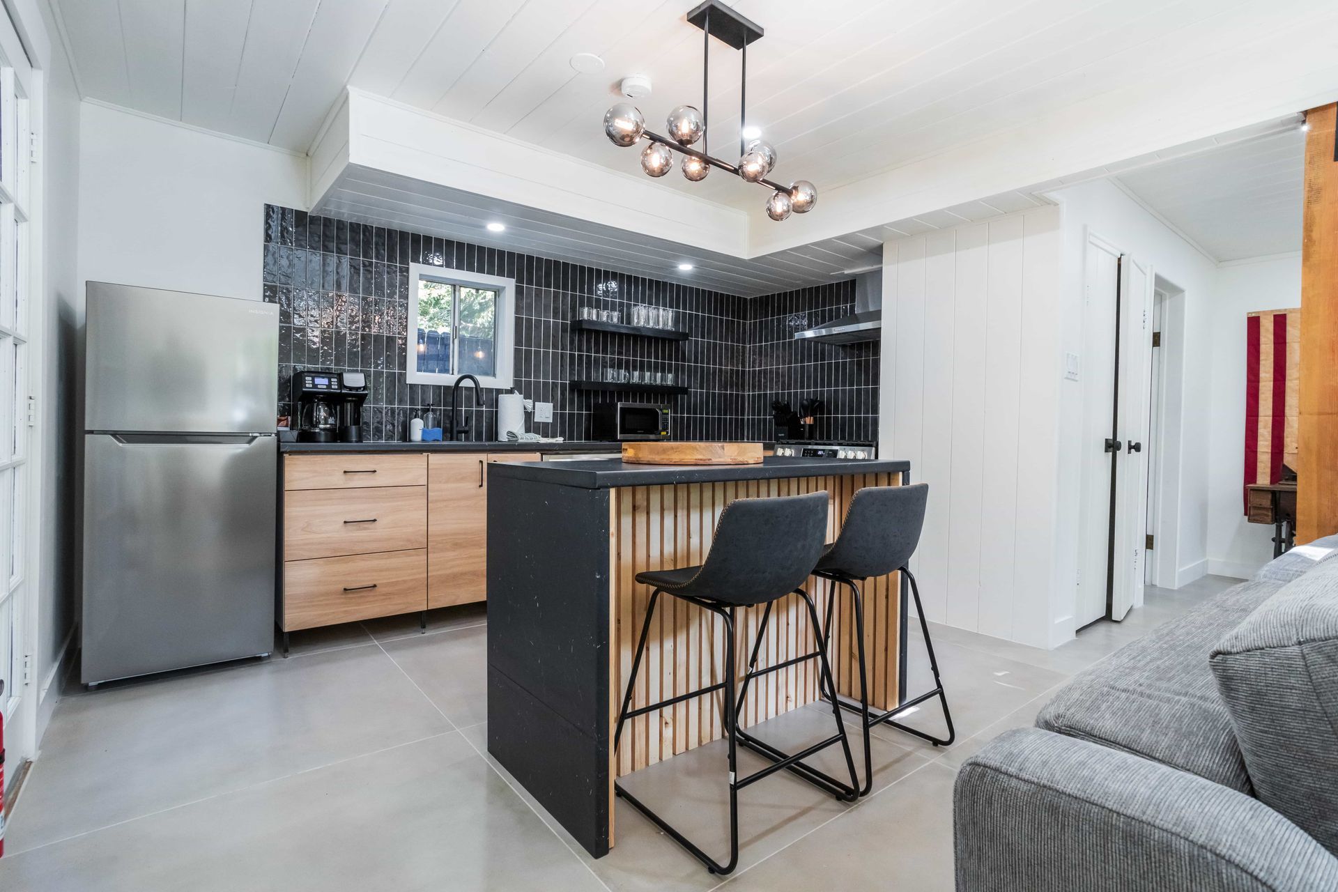A kitchen with a large island , stools , a refrigerator and a couch.