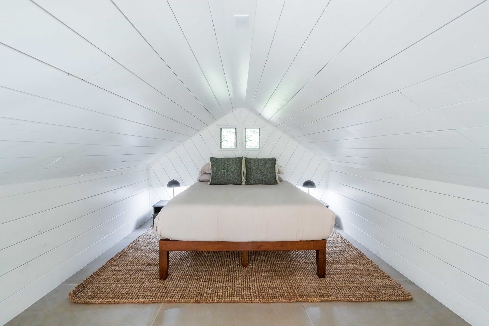 There is a bed in the attic with a rug on the floor.