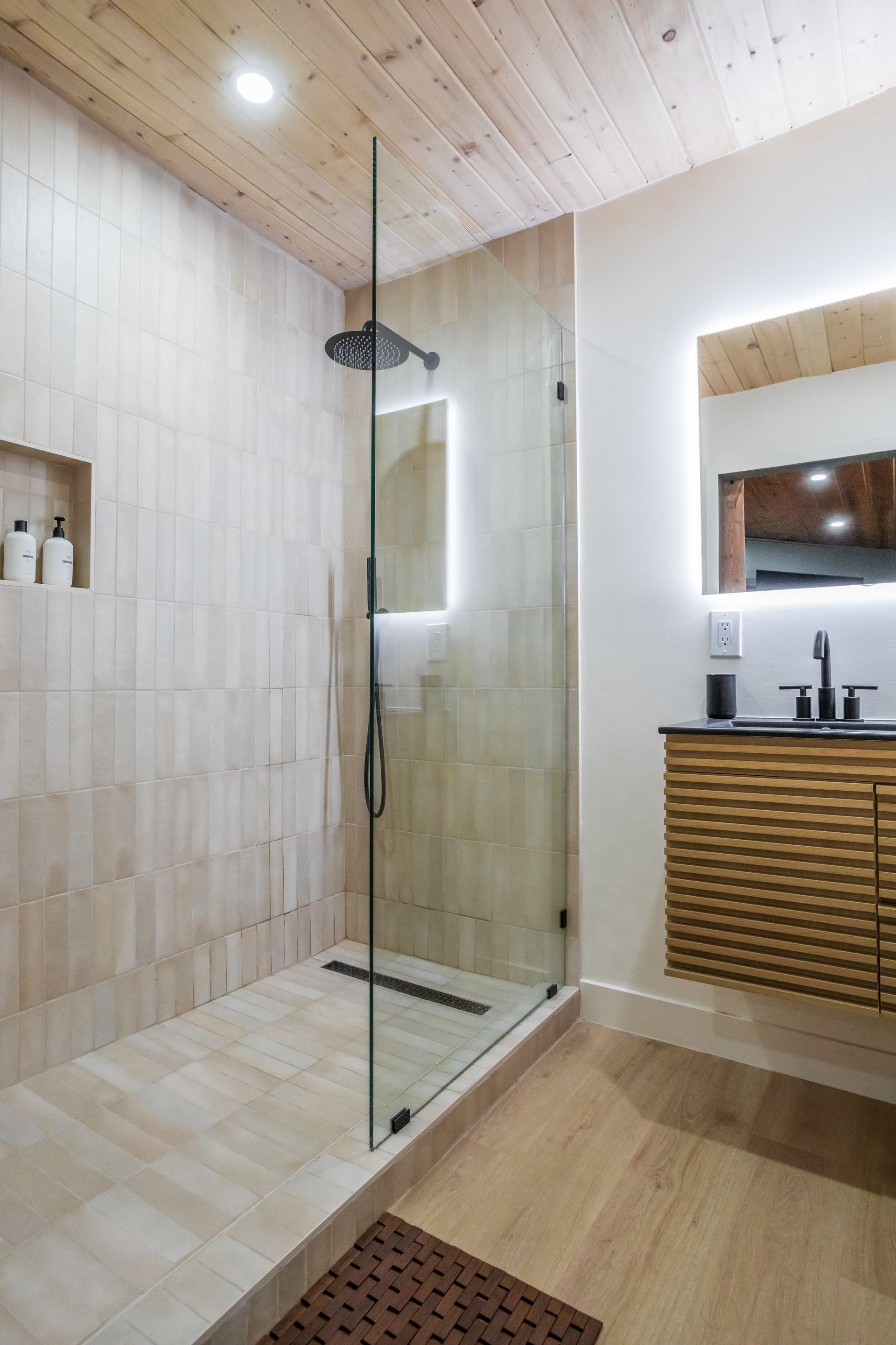 A bathroom with a walk in shower , sink and mirror.