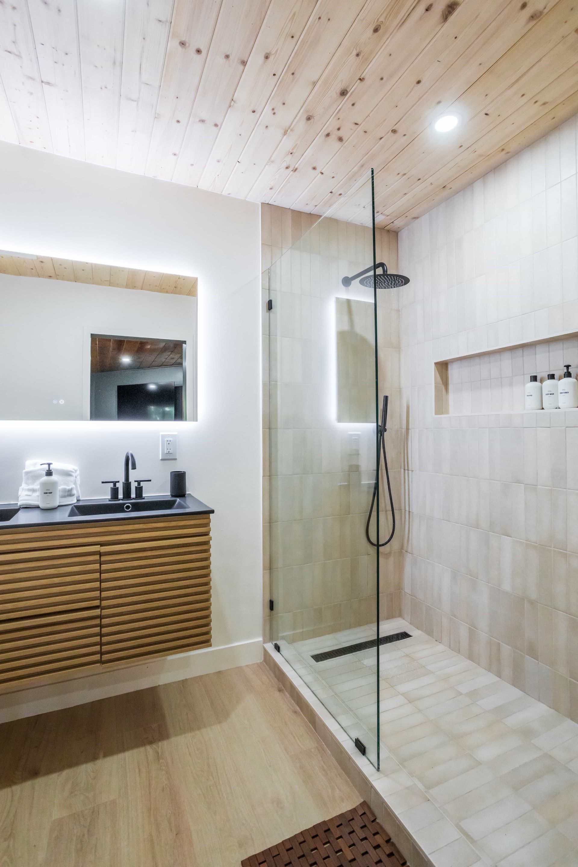 A bathroom with a walk in shower , sink , mirror and wooden ceiling.