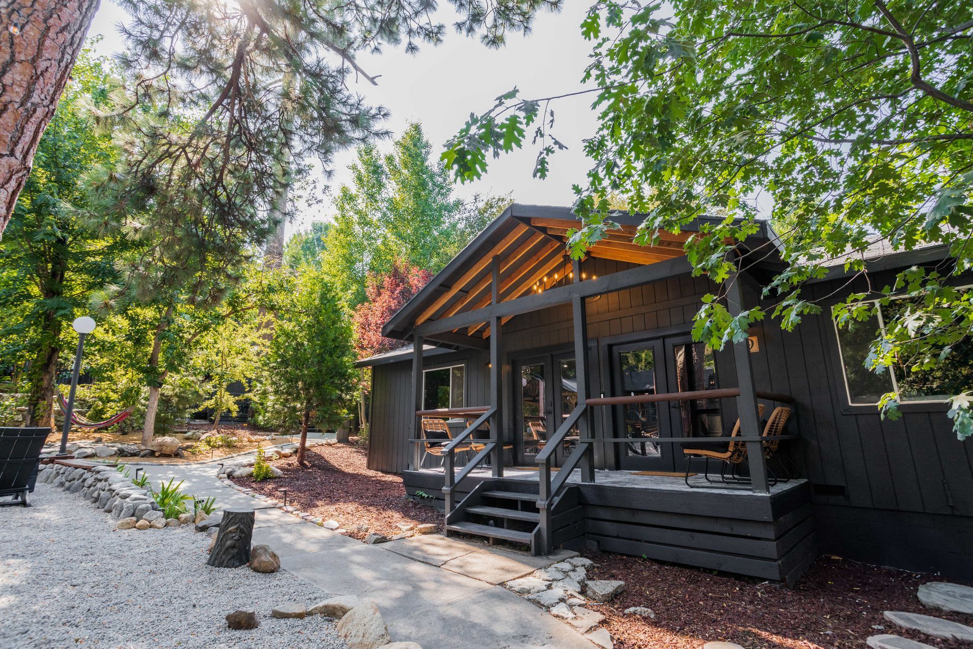 A small black house with a porch in the middle of a forest.