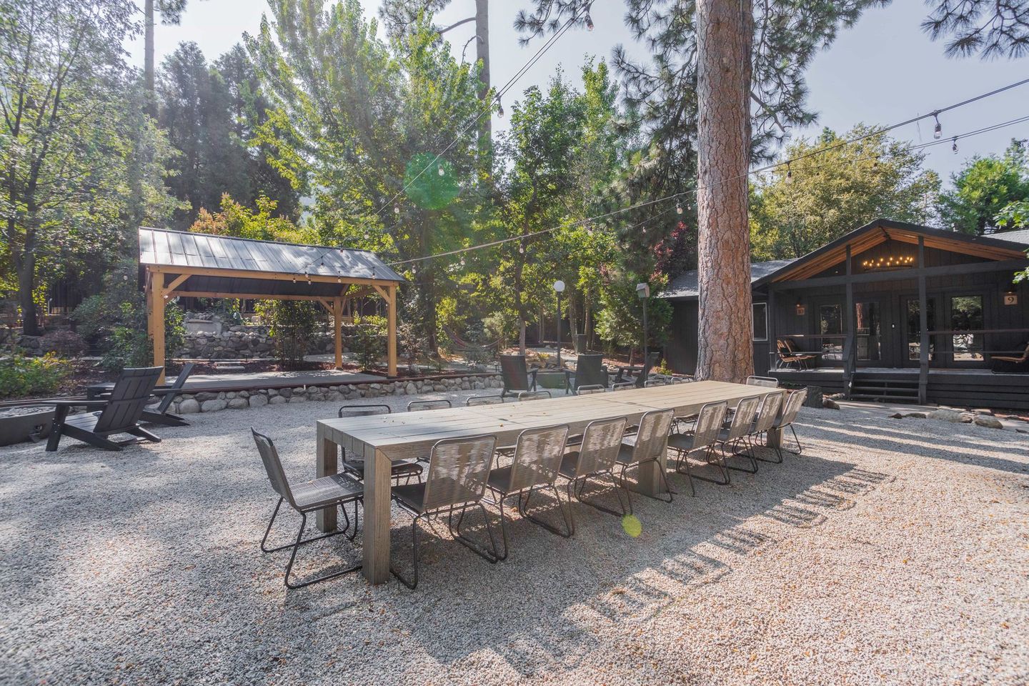 A long wooden table and chairs are sitting in a gravel area in front of a house.