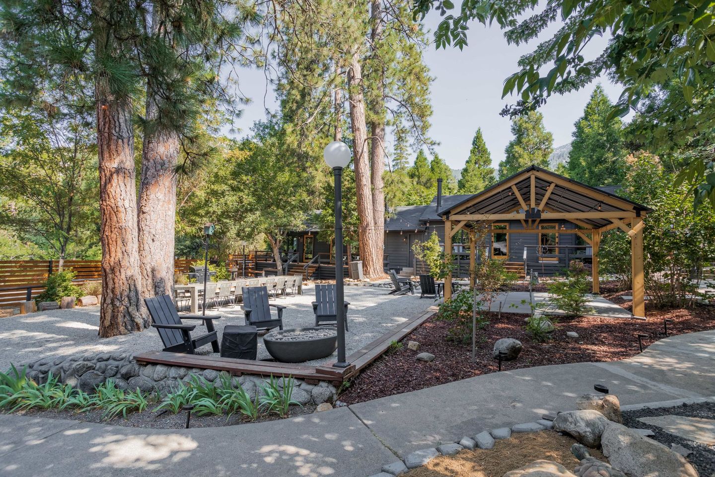 A patio with chairs and tables in front of a house surrounded by trees.