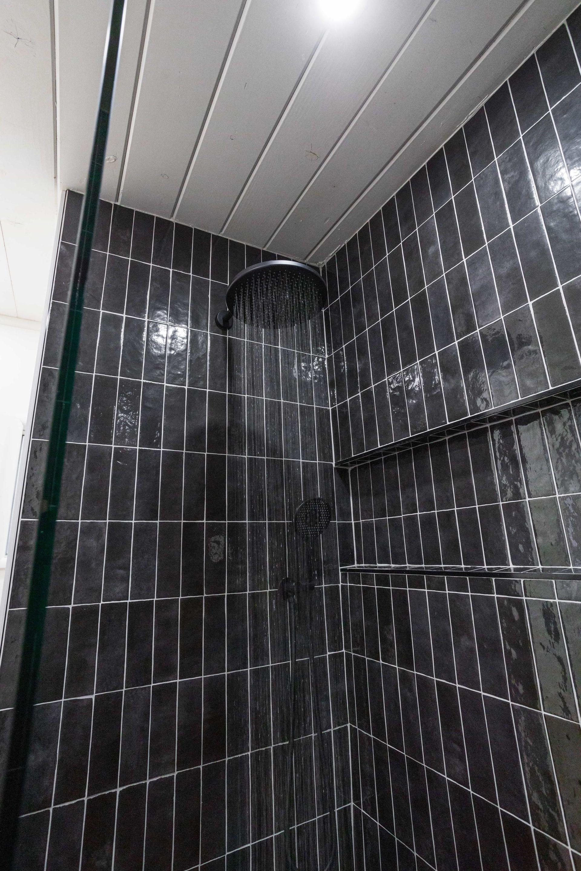 A close up of a shower head in a bathroom with black tiles.