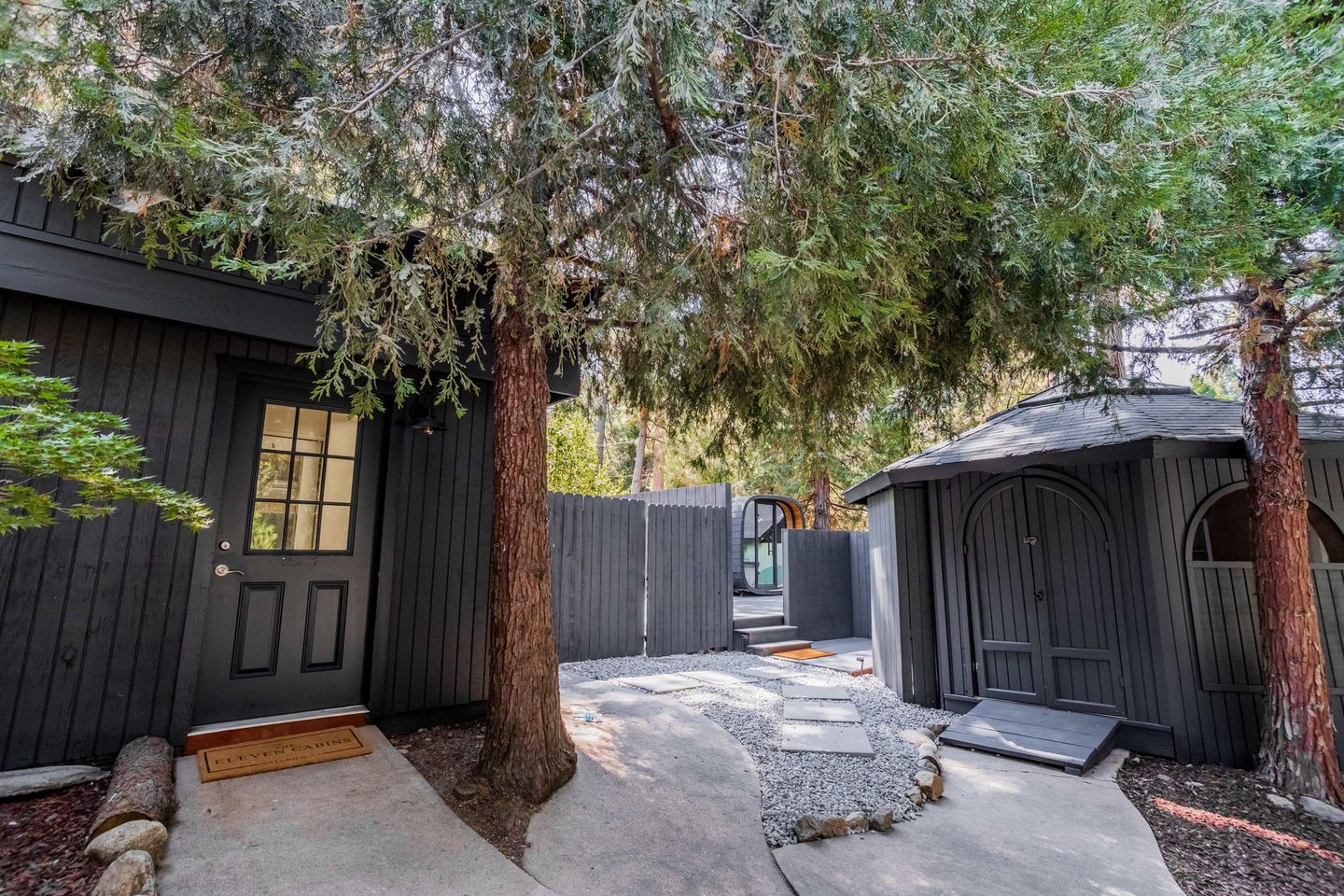 A black house with a fence and trees in front of it.