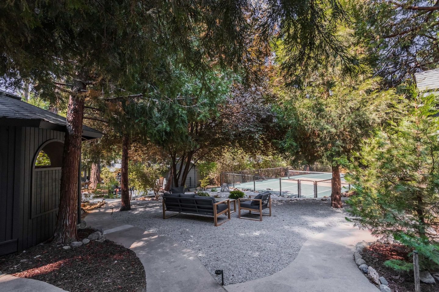 A patio area with a bench , chairs , and trees in front of a house.