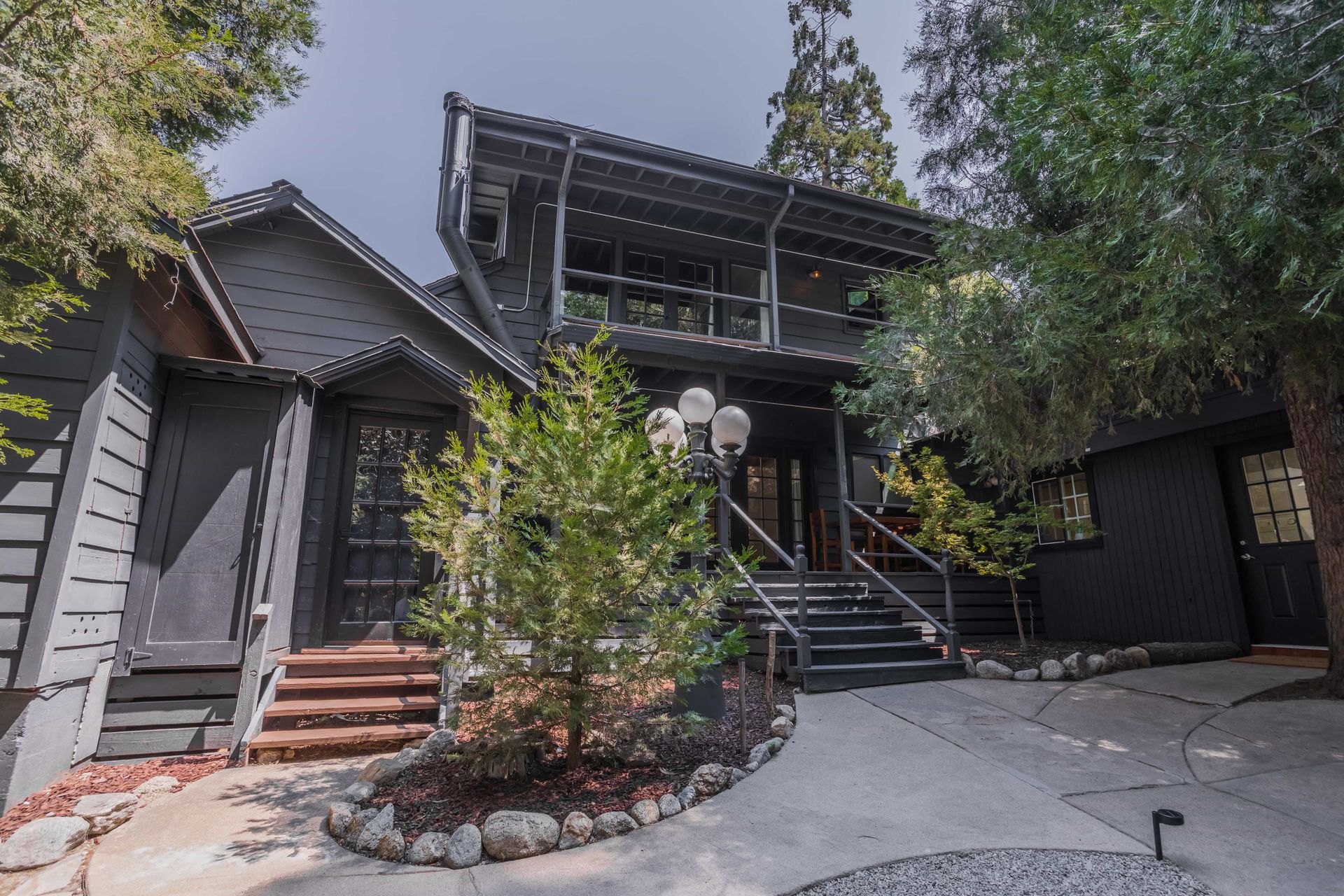 A large black house with stairs leading up to it is surrounded by trees.