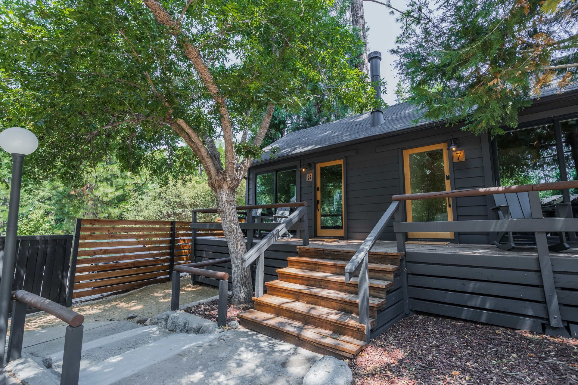A black house with a wooden deck and stairs leading up to it.
