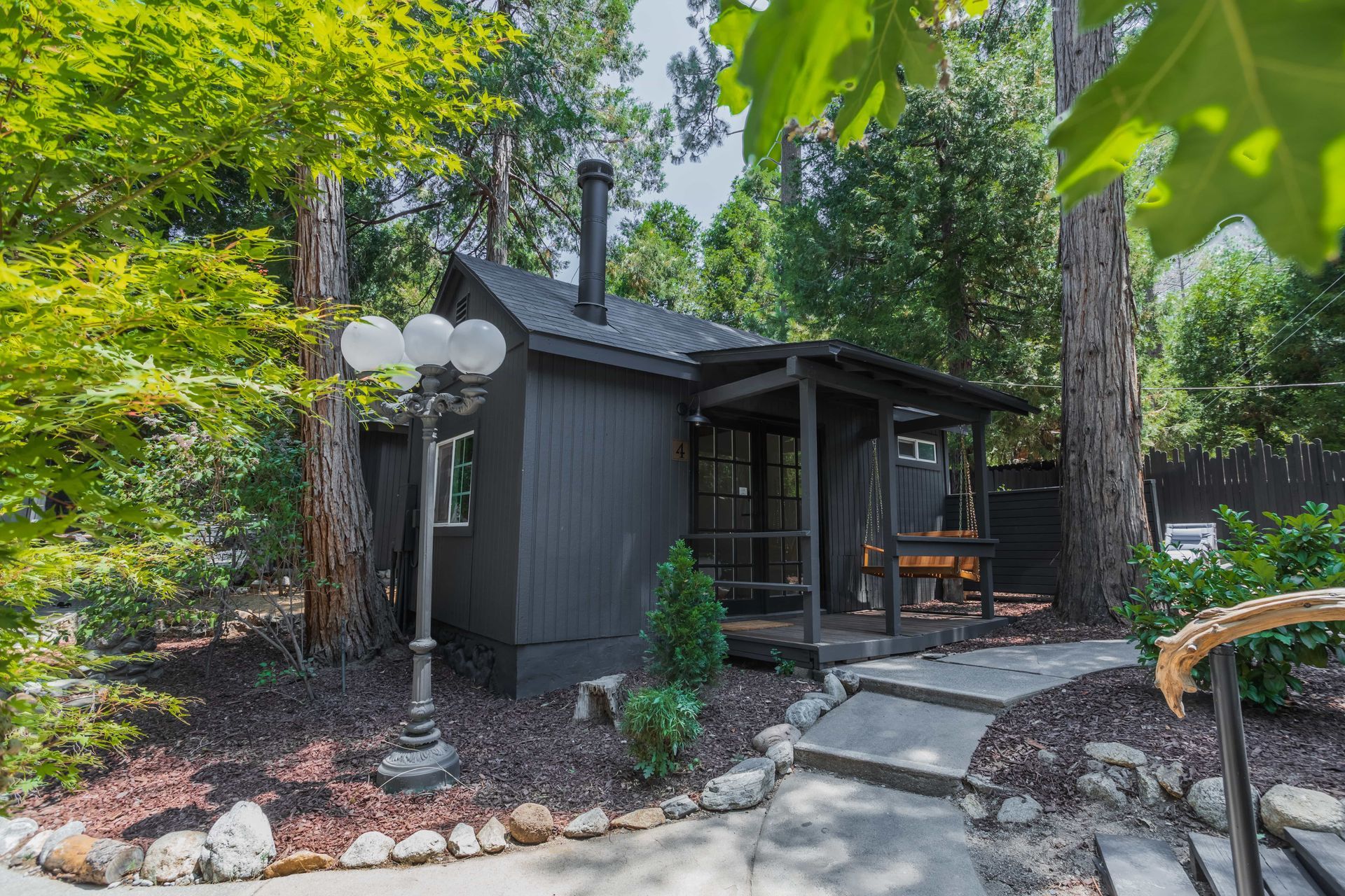 A small black house with a porch is surrounded by trees.