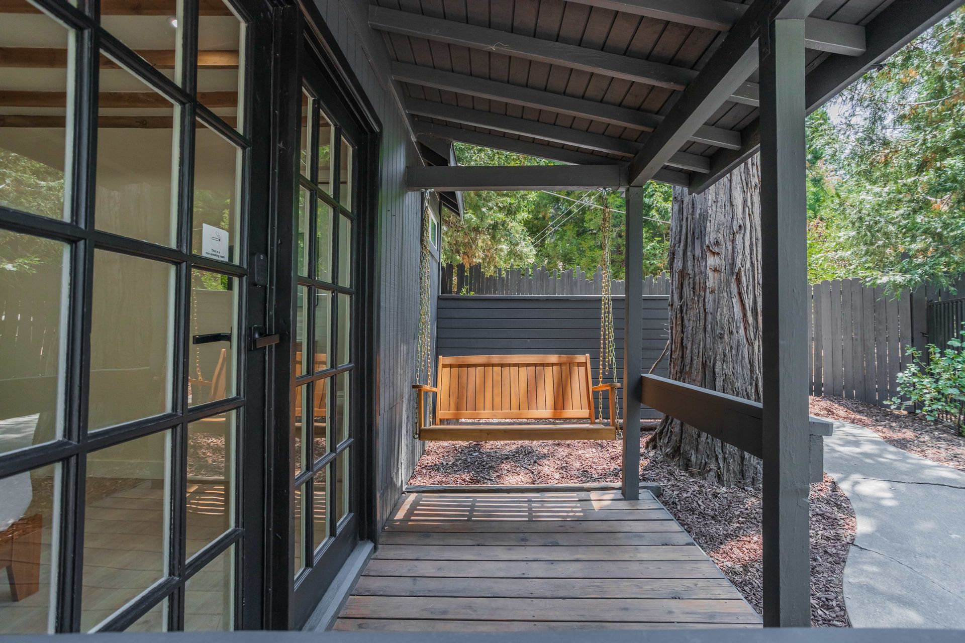 There is a porch with a swing and a fence in the background.