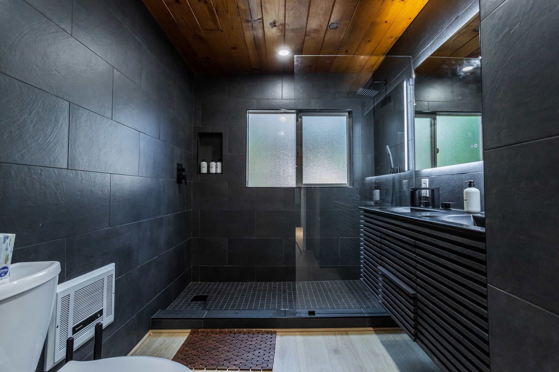 A bathroom with black tiles and a walk in shower.