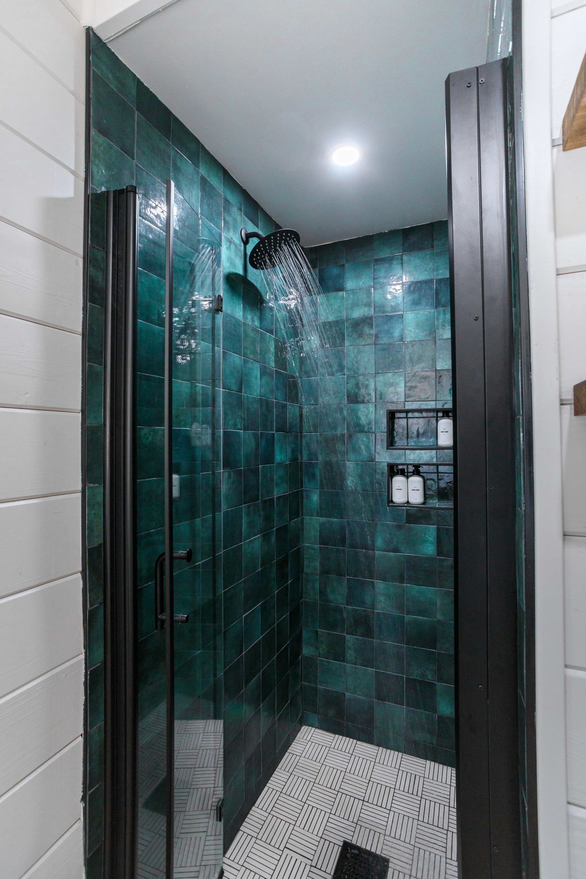 A bathroom with green tiles and a walk in shower with a glass door.